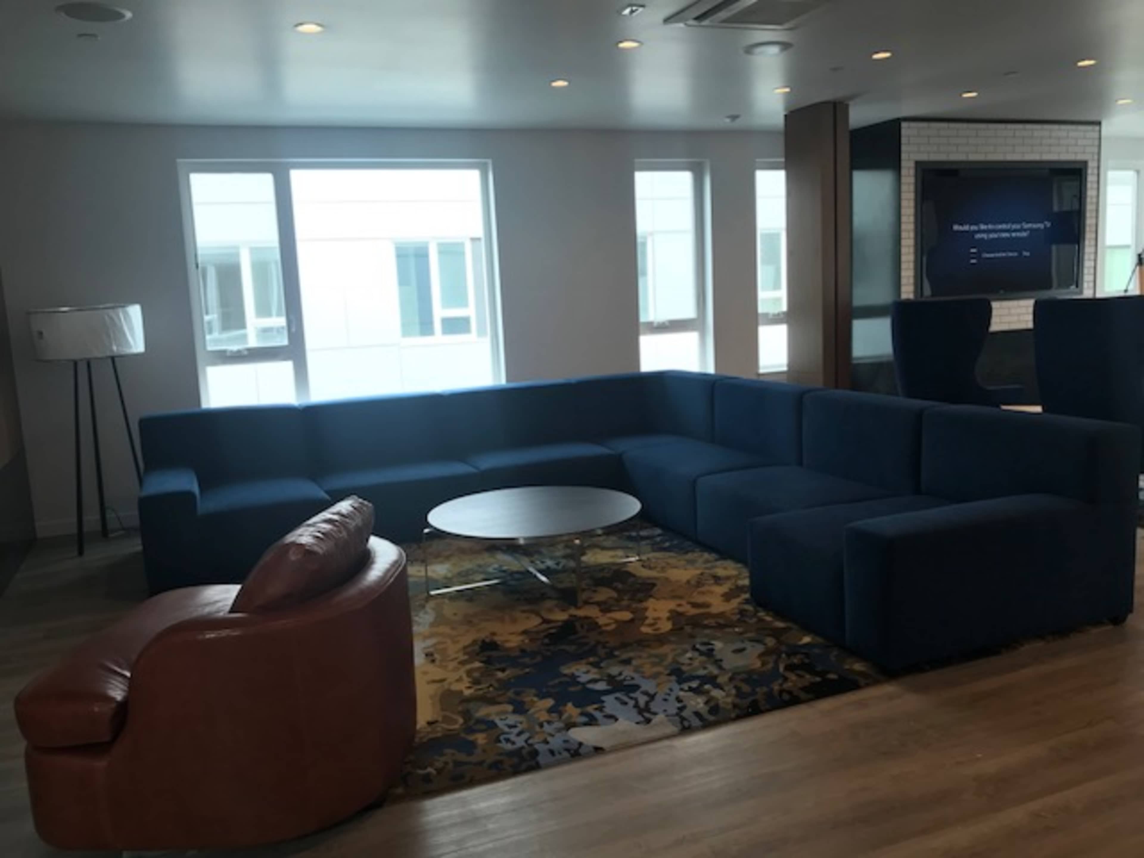 A modern lounge area featuring a large navy blue sectional sofa, a brown leather armchair, a round coffee table, and a patterned rug on a wooden floor.