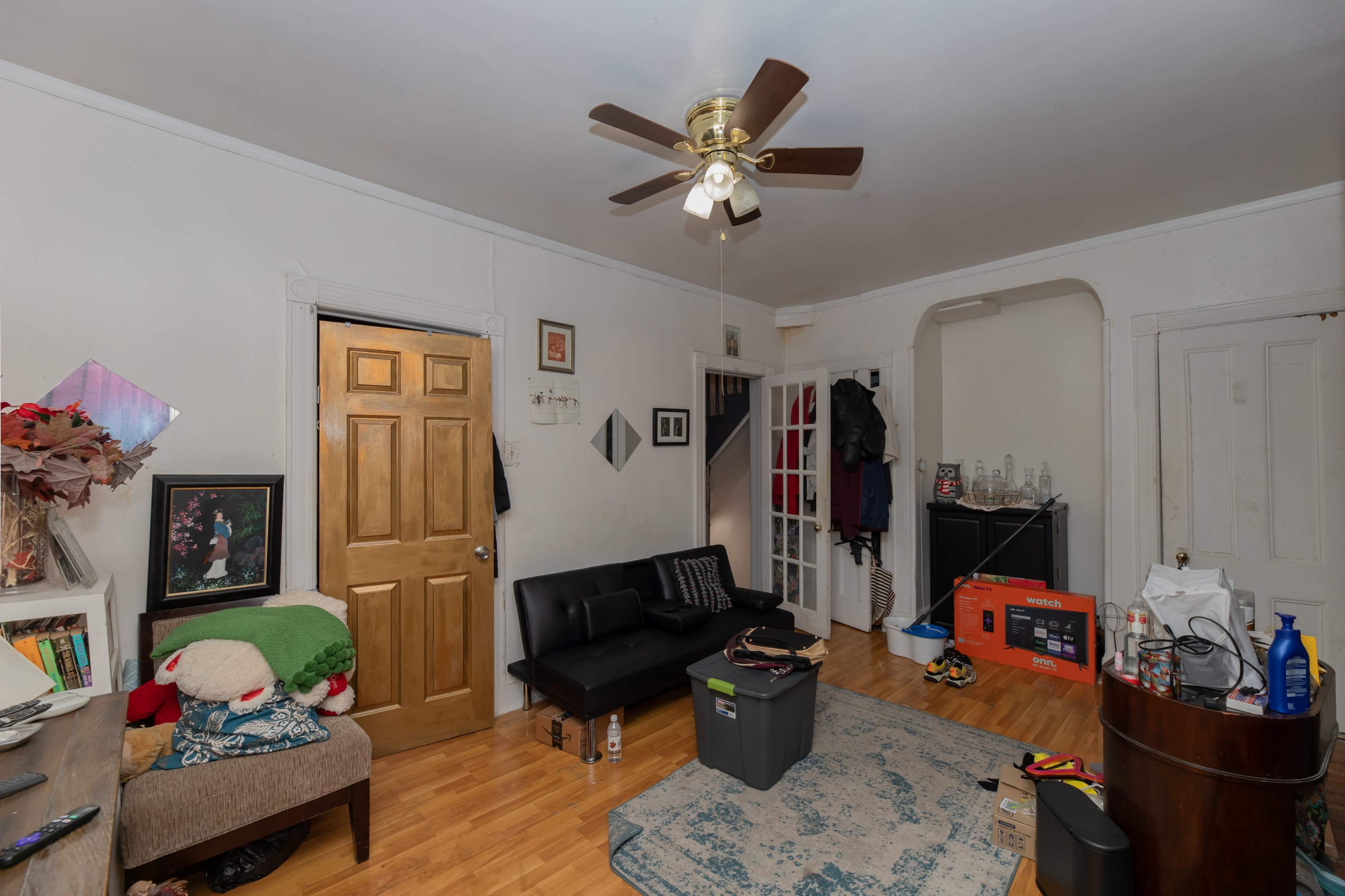 The room features a black couch, a wooden door, and various items scattered throughout, including a storage container and an orange box.