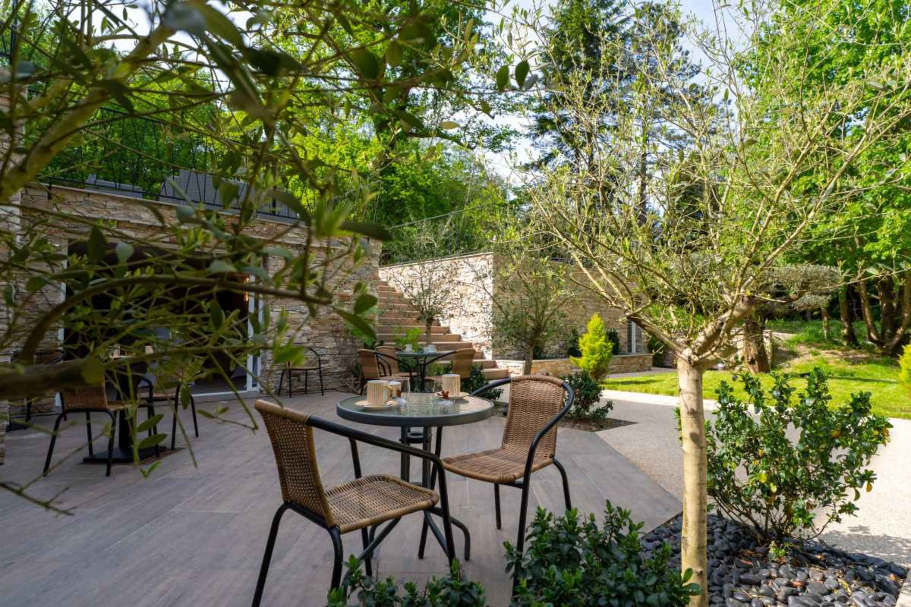 A neatly arranged outdoor seating area features a table with two chairs, surrounded by greenery and stone pathways.
