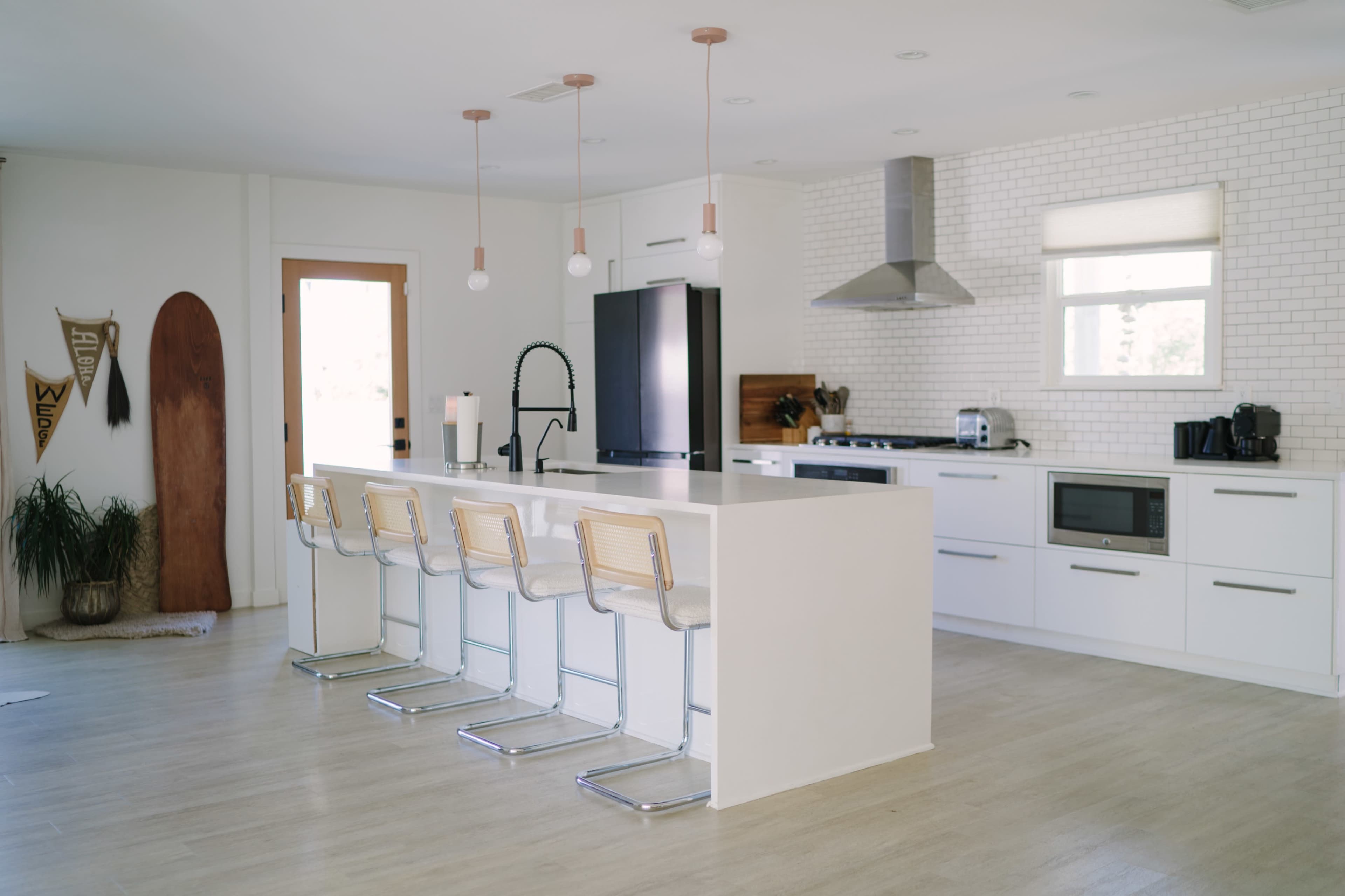 A modern kitchen features a large white island with bar stools, stainless steel appliances, and a wall of white brick.