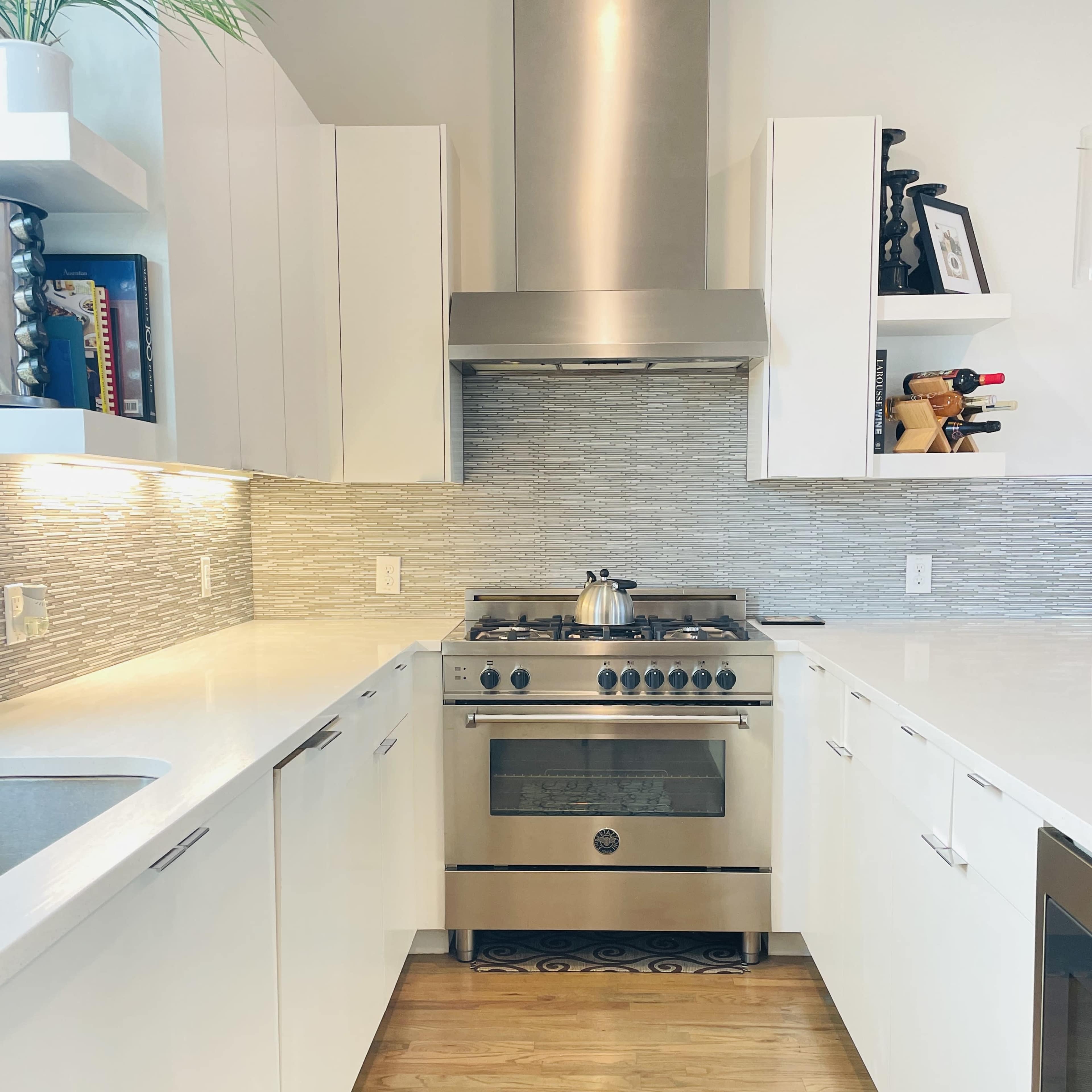 A modern kitchen features white cabinetry, a stainless steel stove with a hood, and a tiled backsplash.