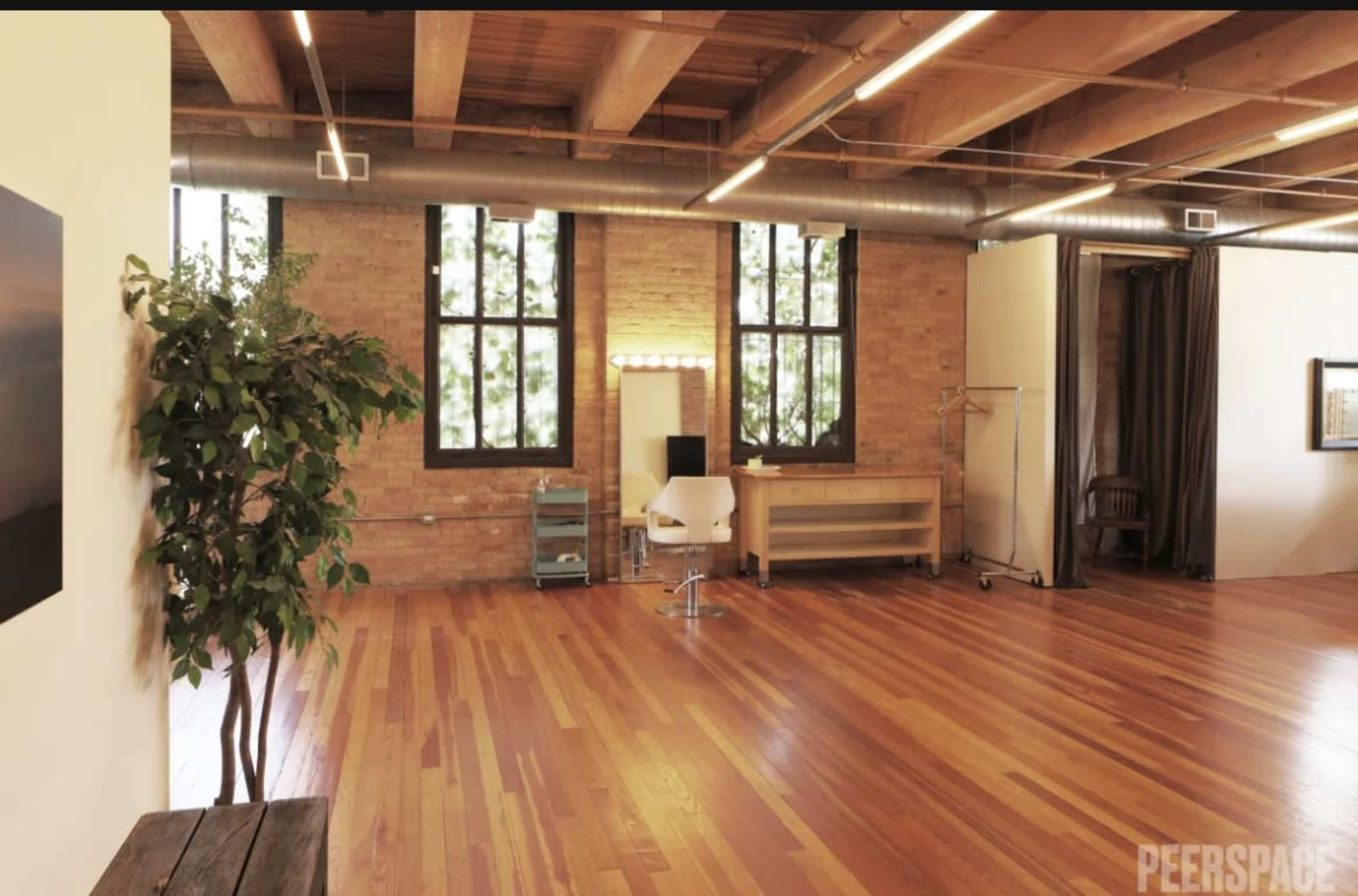 A spacious room with wooden floors, large windows, a makeup station with lights, and a clothing rack.
