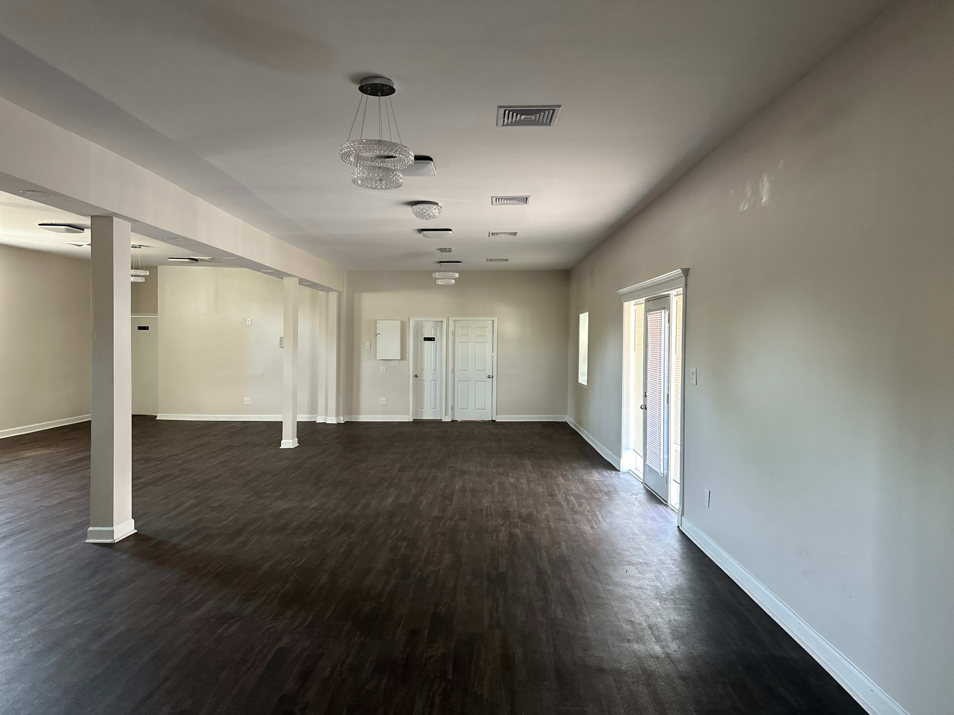 A spacious, empty room with wood-like flooring, white walls, and several decorative light fixtures hanging from the ceiling.