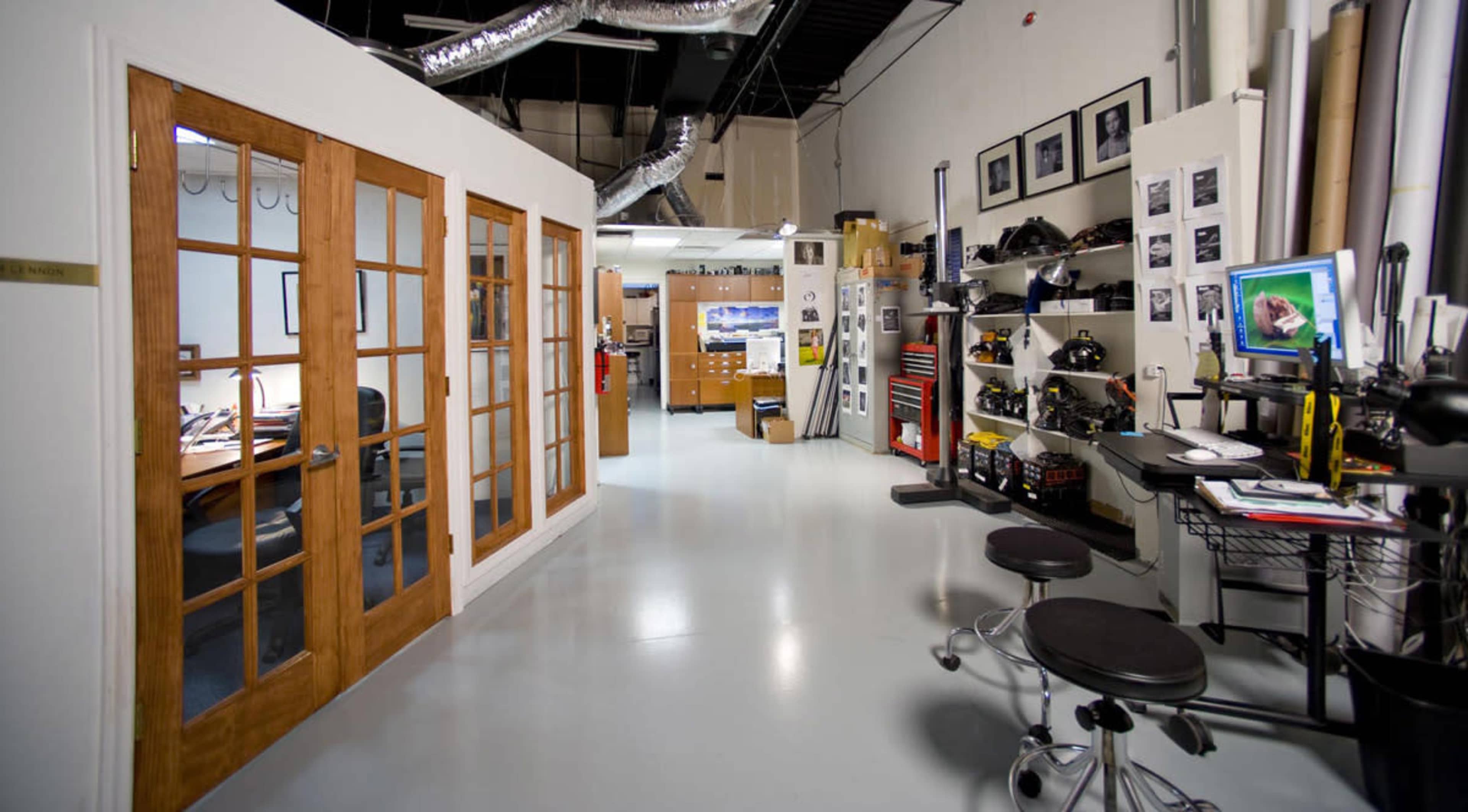 An office space with a glass door section leading to a workspace, equipped with desks, filing cabinets, and various office equipment.