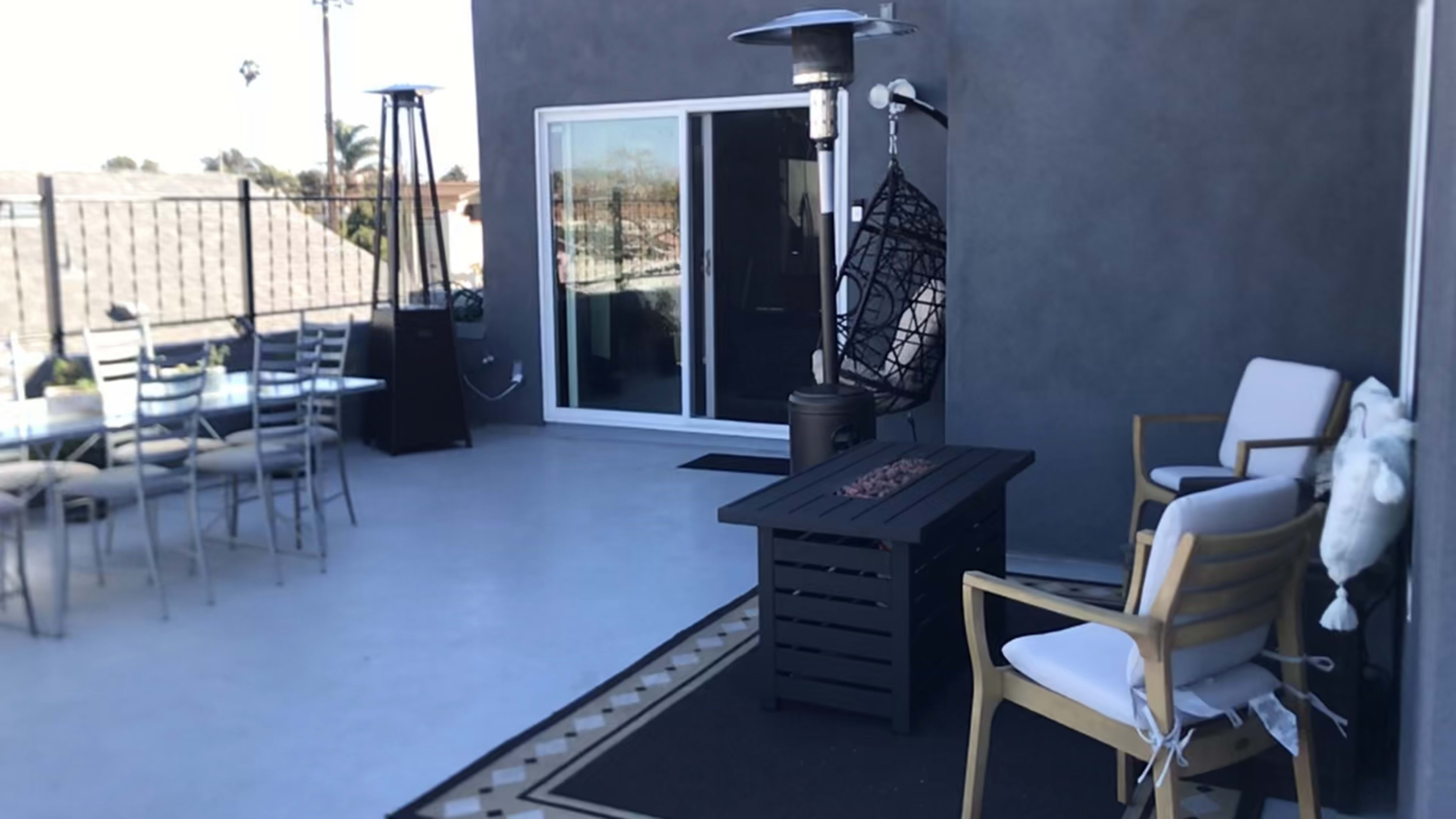 A modern rooftop terrace with a seating area, a small table, and patio heaters in the background.