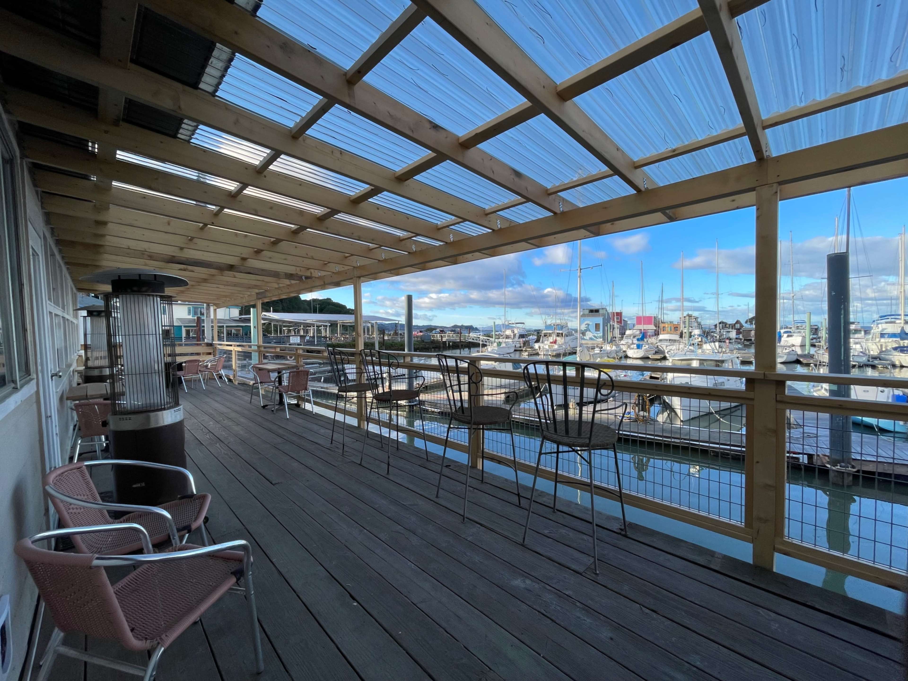 A covered wooden deck with metal chairs overlooks a marina filled with boats.