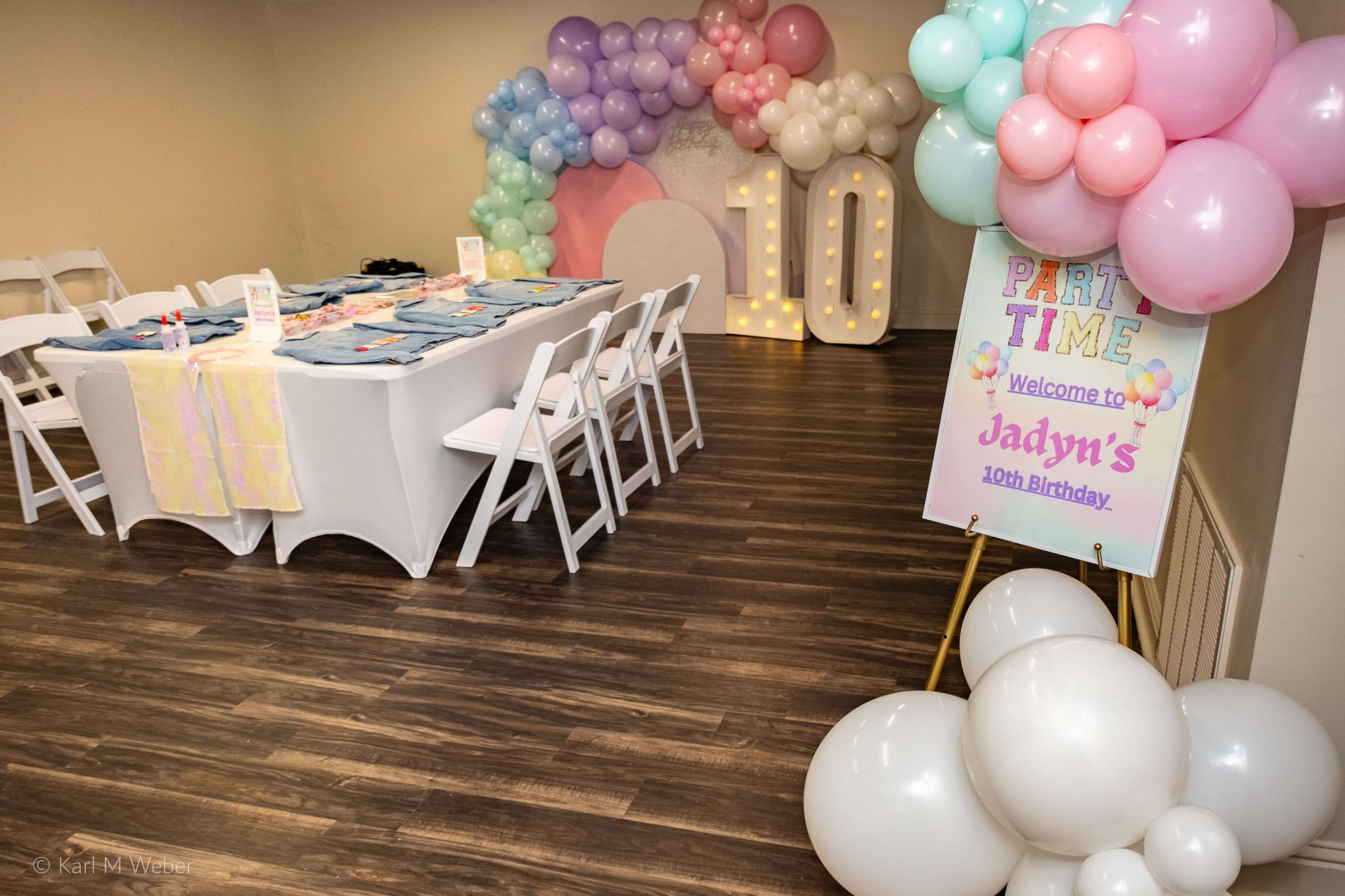 The image shows a decorated party space with a table set for a birthday celebration, colorful balloons, and a sign welcoming guests to Jadyn's 10th birthday.