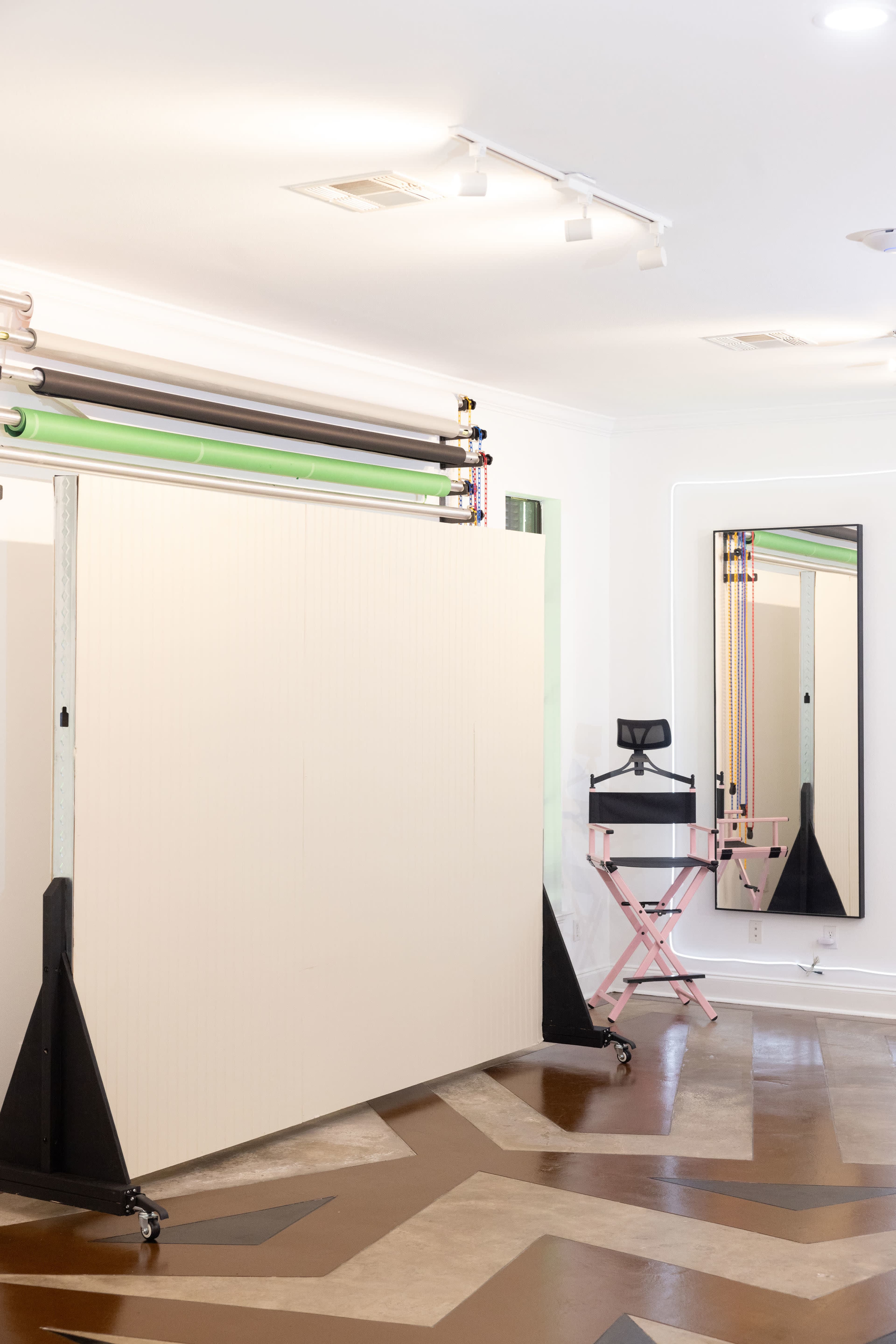 The image shows a well-lit studio space featuring a seamless backdrop setup, a makeup station with a chair, and a large mirror.