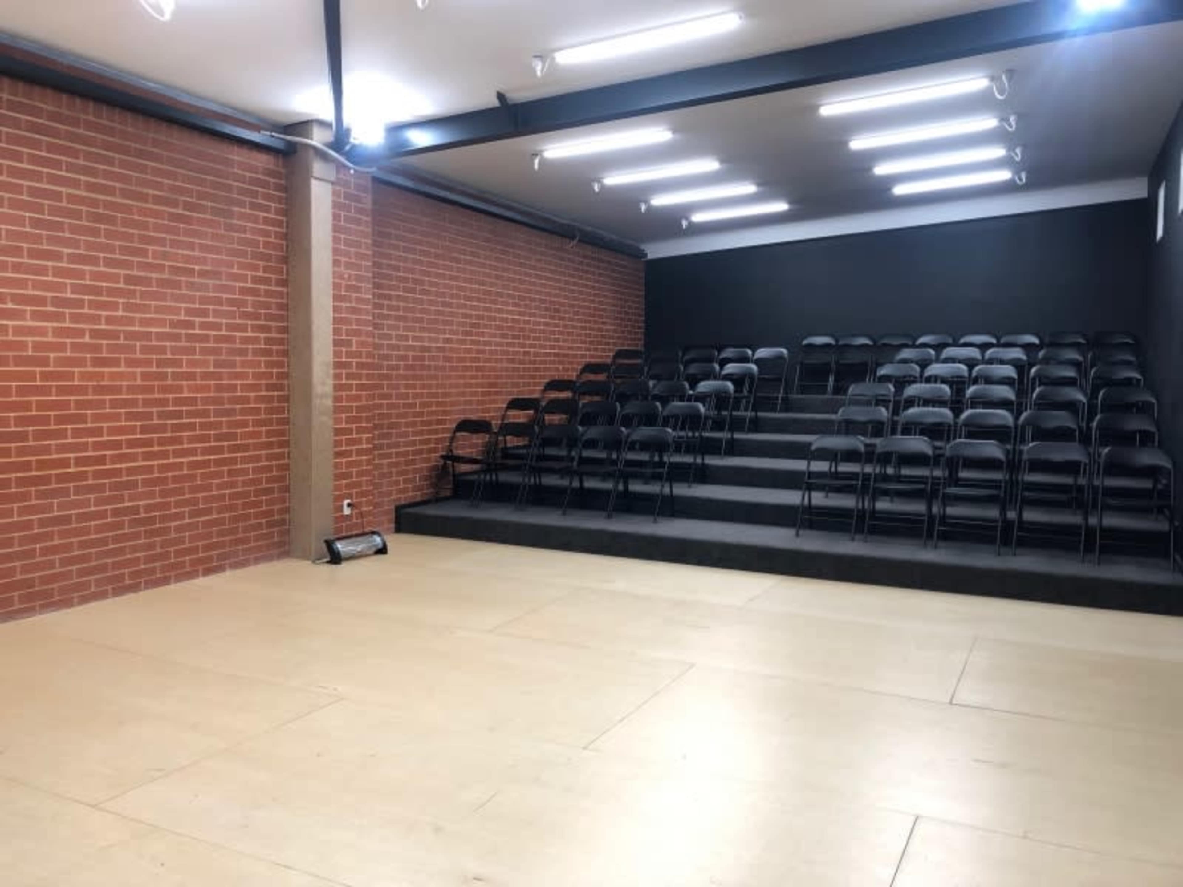A rectangular room with a brick wall and tiered seating made of black chairs facing a blank wall.