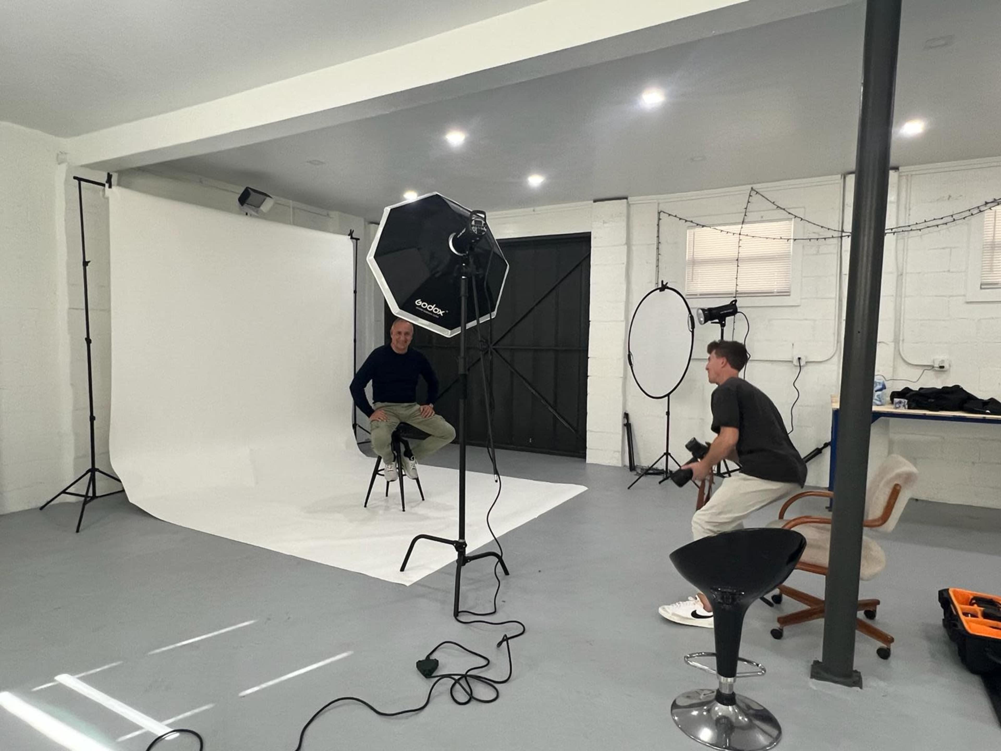 A photography studio features a backdrop, lighting equipment, and two individuals preparing for a photo session.
