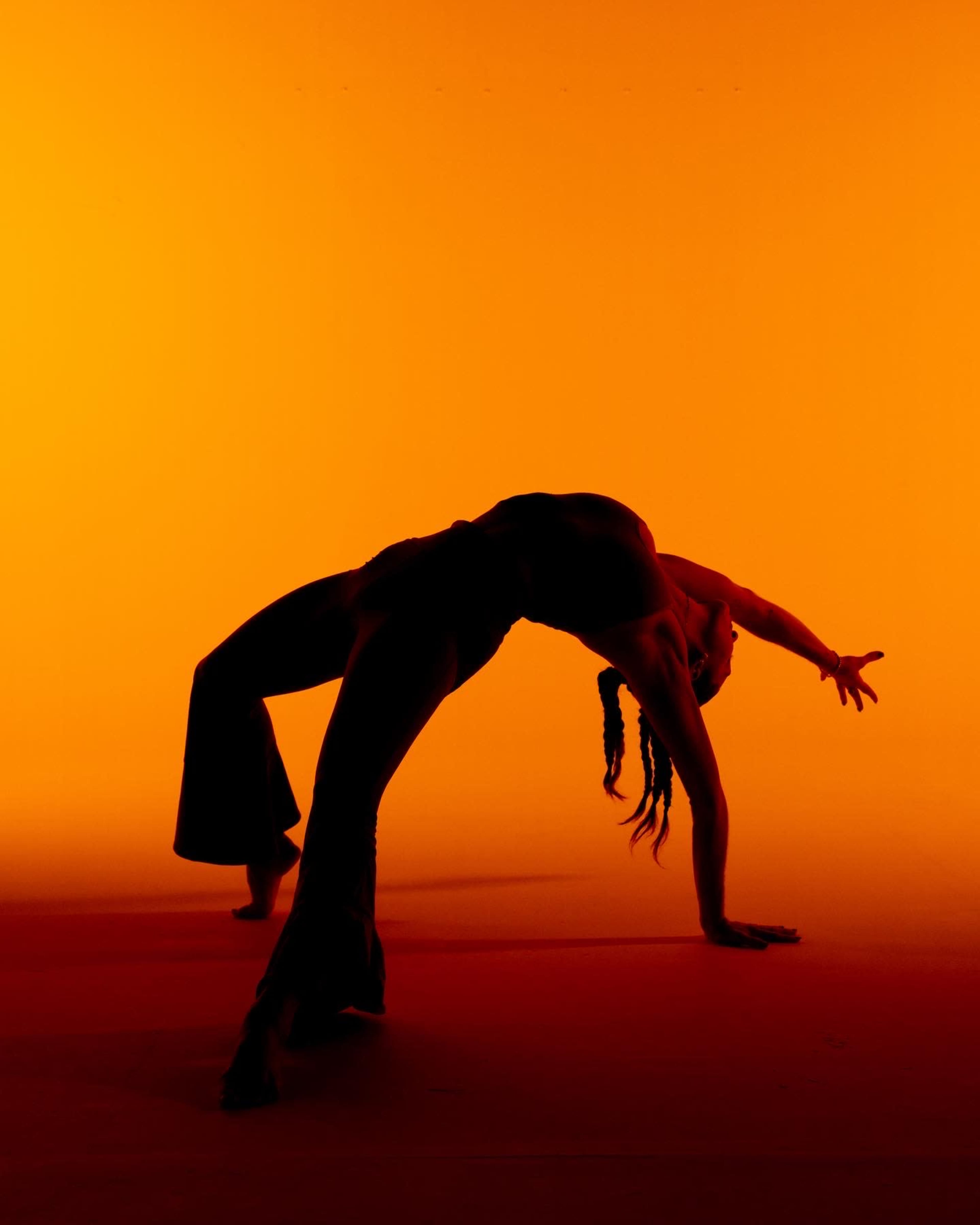 A dancer performs a backbend against an orange backdrop.