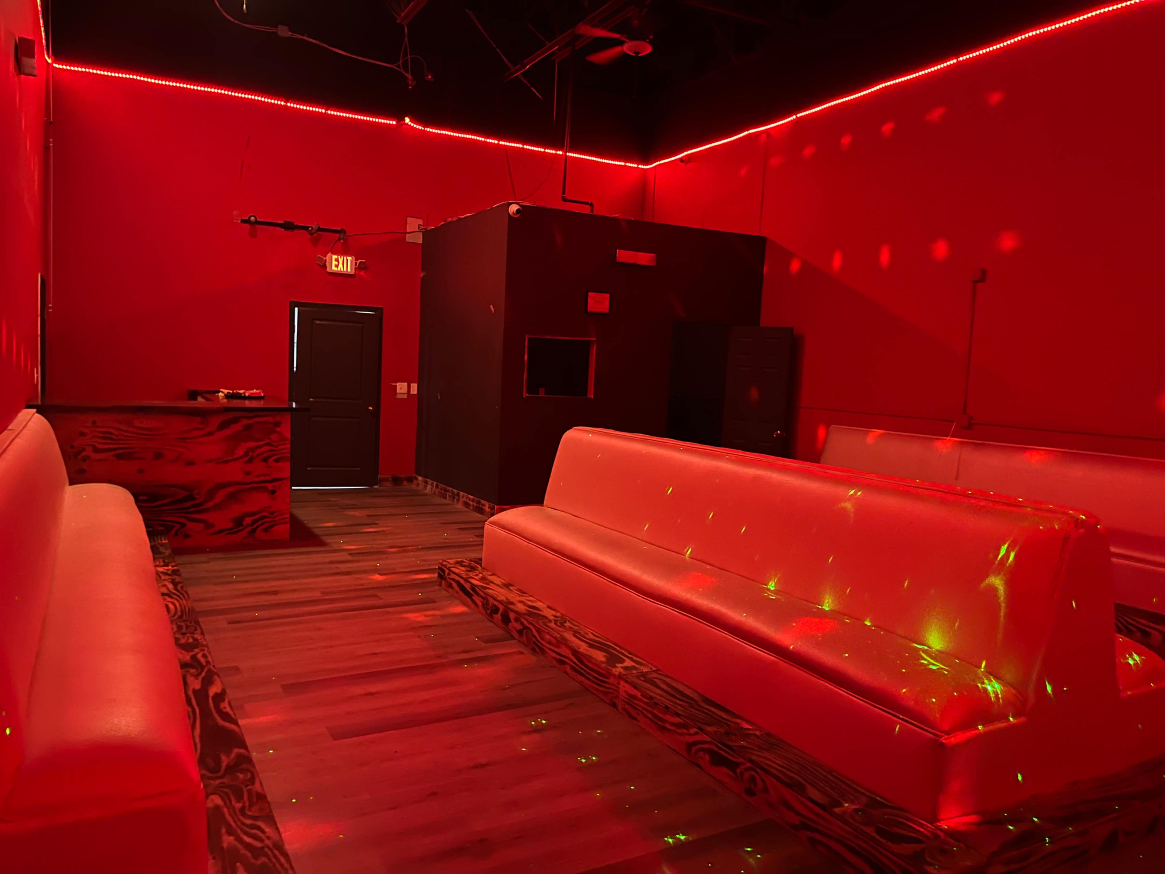 A dimly lit room features red walls and couches, with a bar area and decorative lighting effects on the floor.