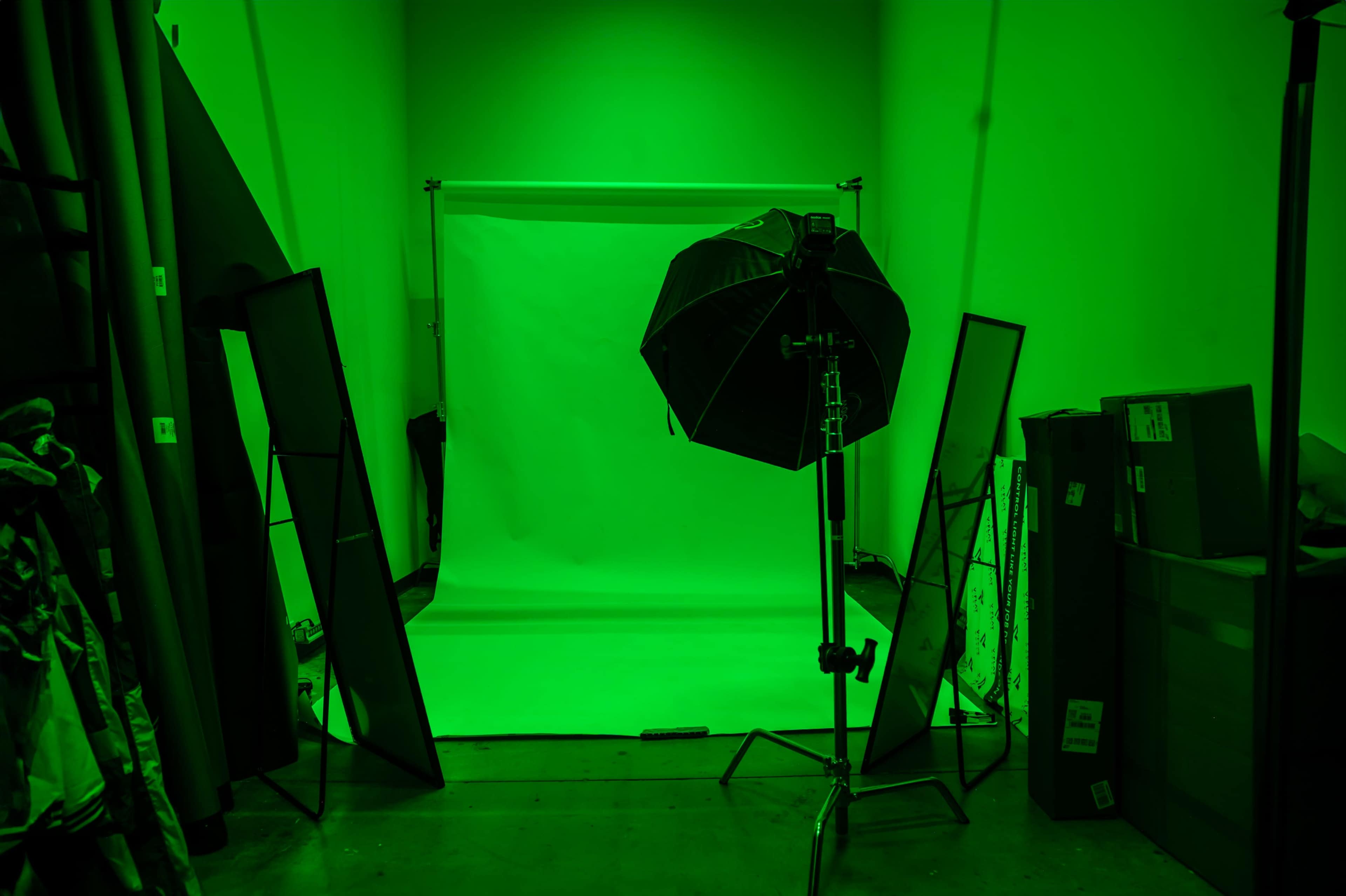 The image shows a green-lit photography studio with a backdrop, lighting equipment, and reflective stands arranged around the space.