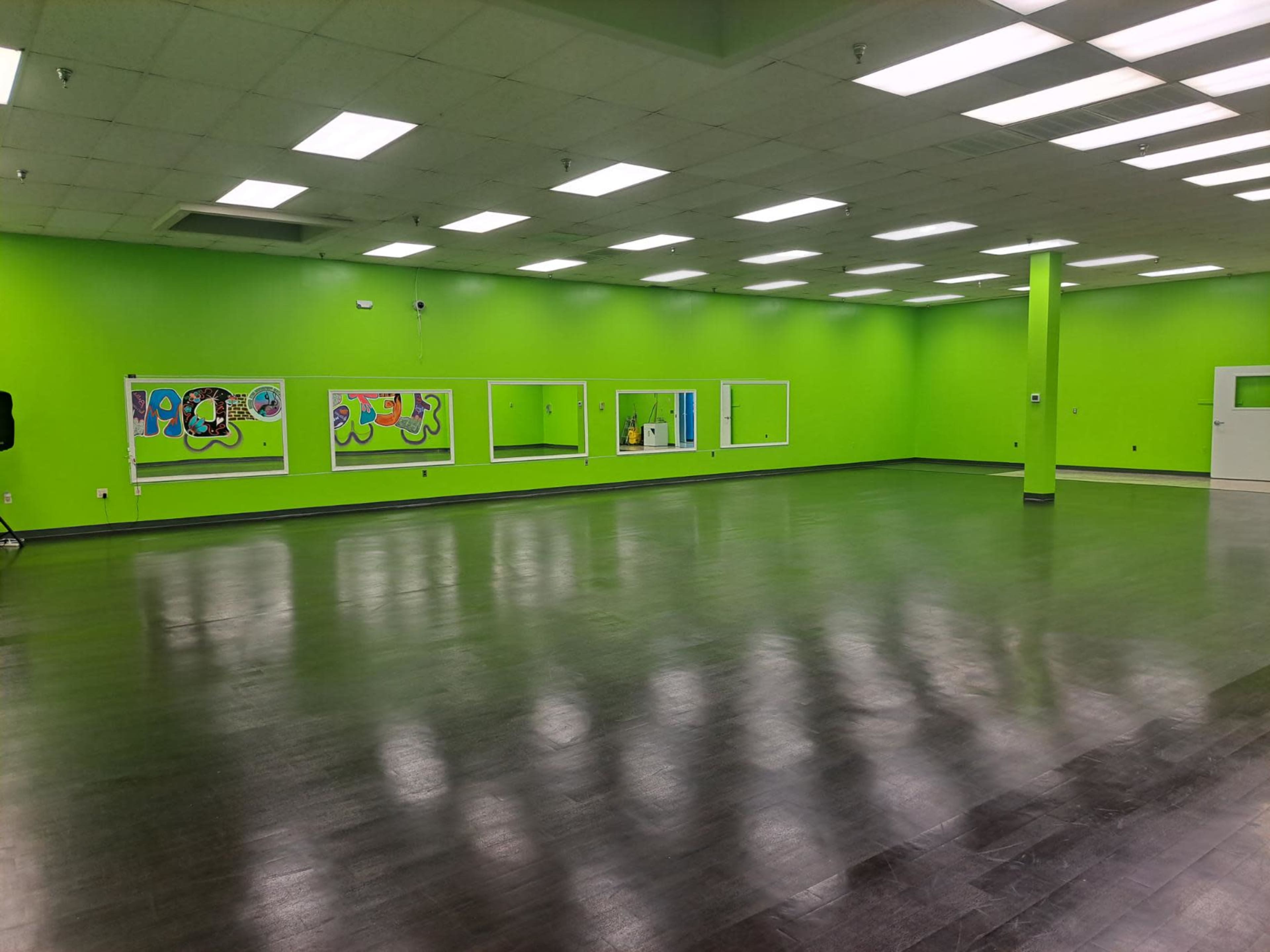 A spacious room with bright green walls, large mirrors, and a polished dark wood floor.