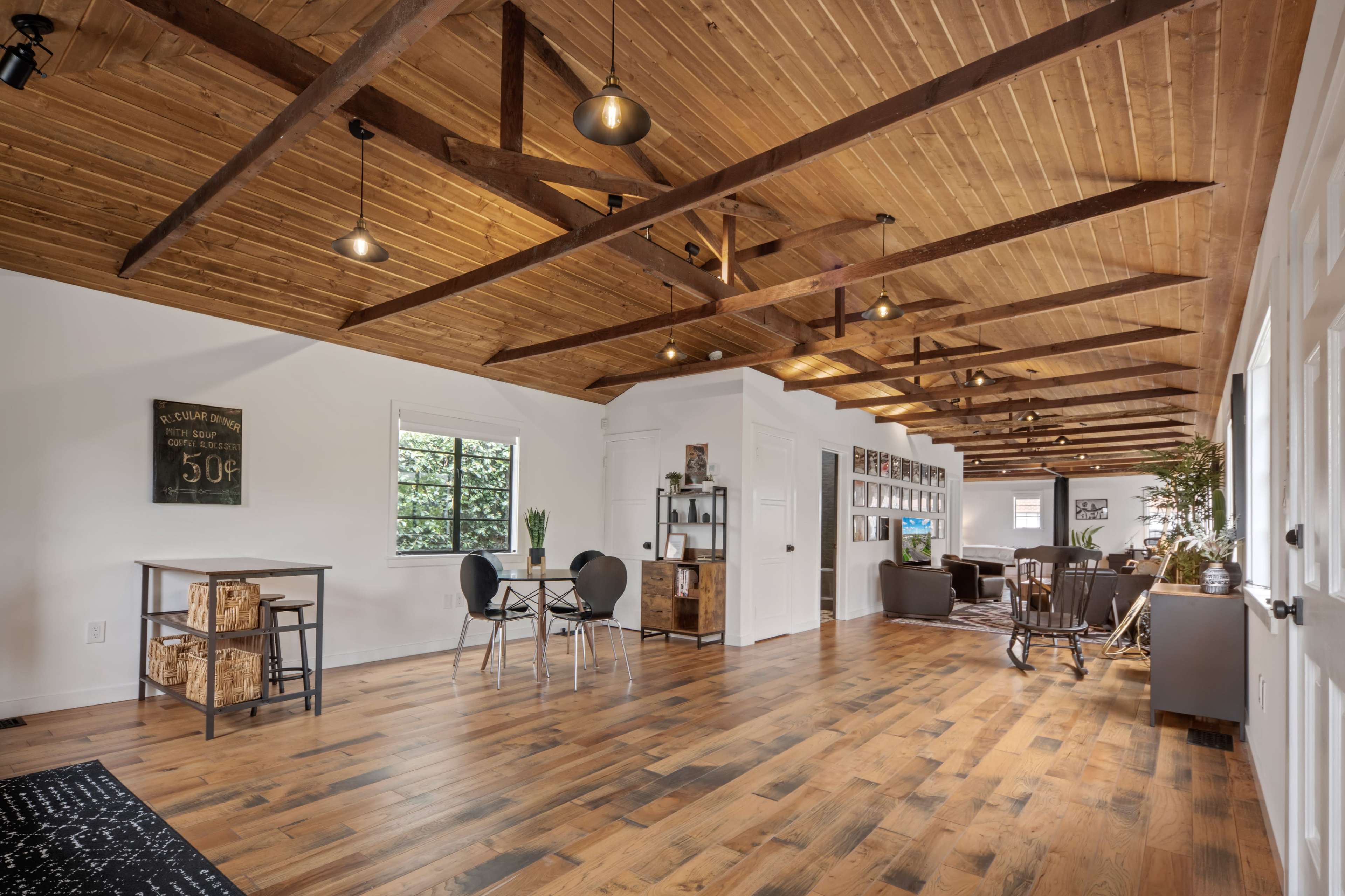 A spacious room with wooden beams, a wooden floor, and modern furniture arranged for relaxation and dining.