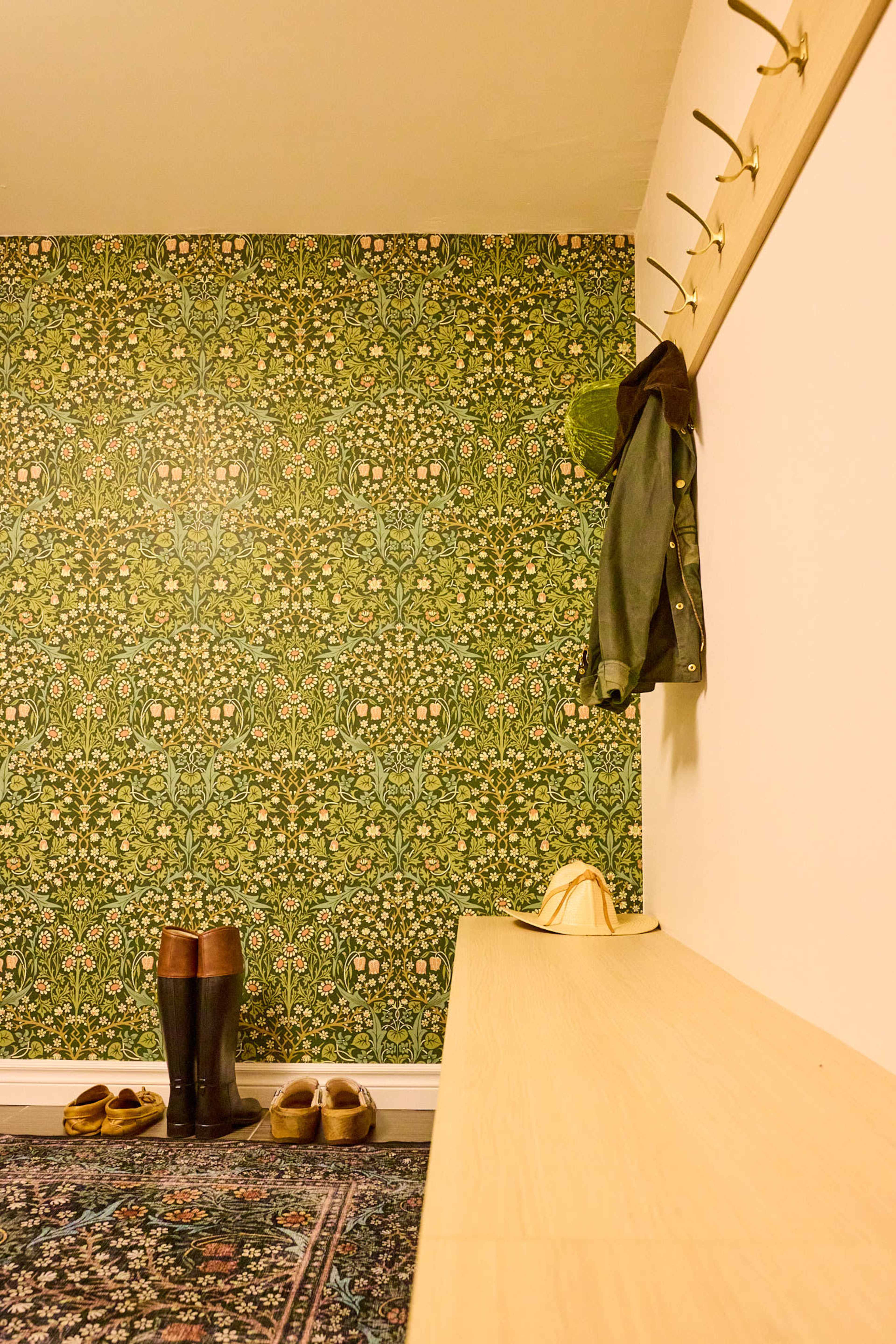 A green-patterned wall is complemented by a wooden bench, shoes, and a coat hanging on hooks.