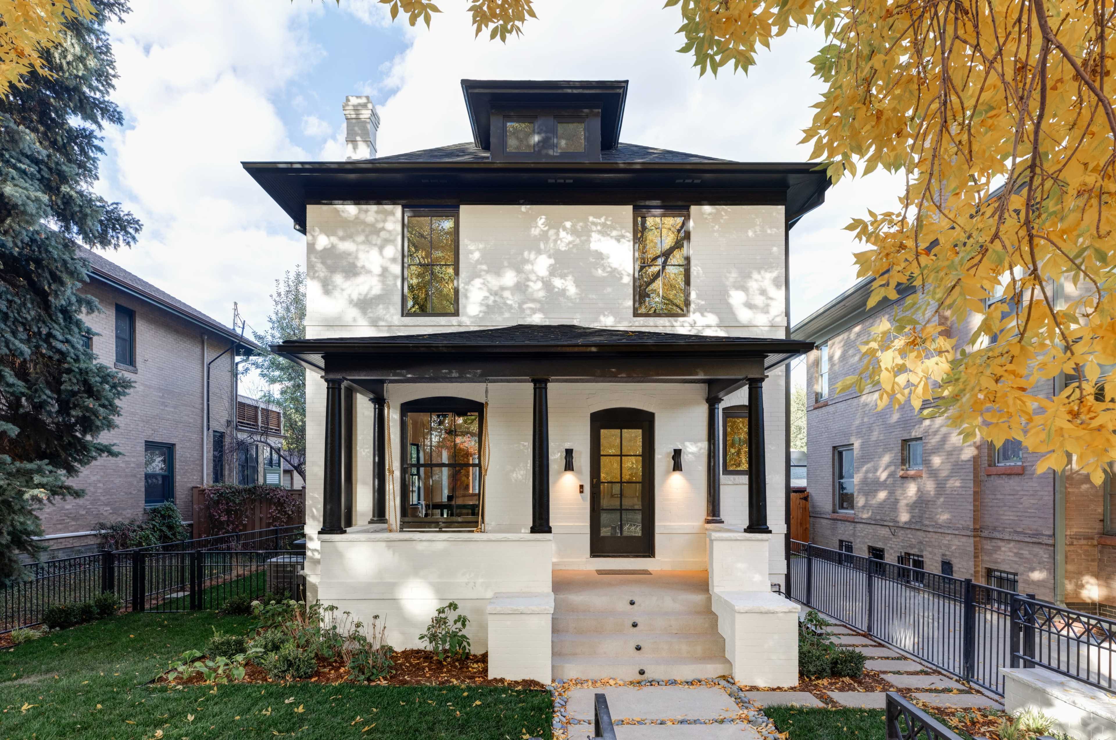 A two-story house with a white exterior, black trim, and a front porch surrounded by autumn leaves.