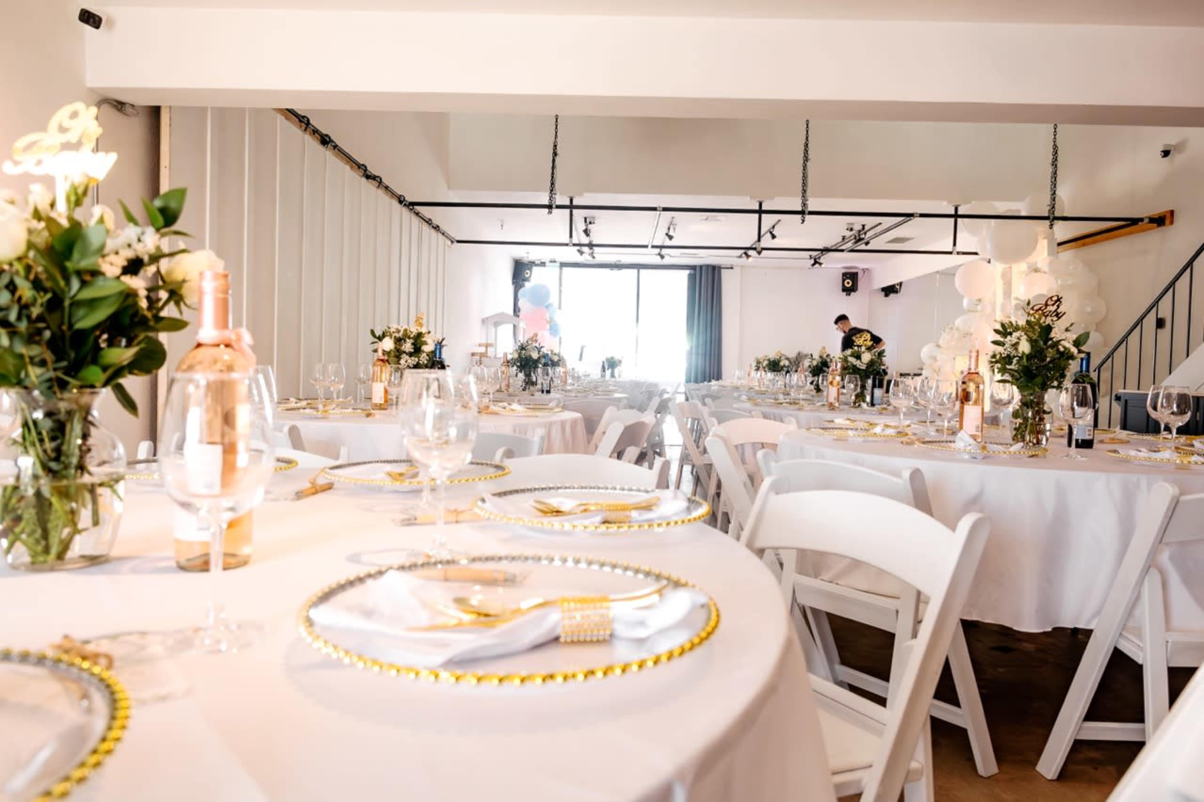 A banquet hall set with elegantly arranged tables adorned with white tablecloths, gold-rimmed plates, and floral centerpieces.