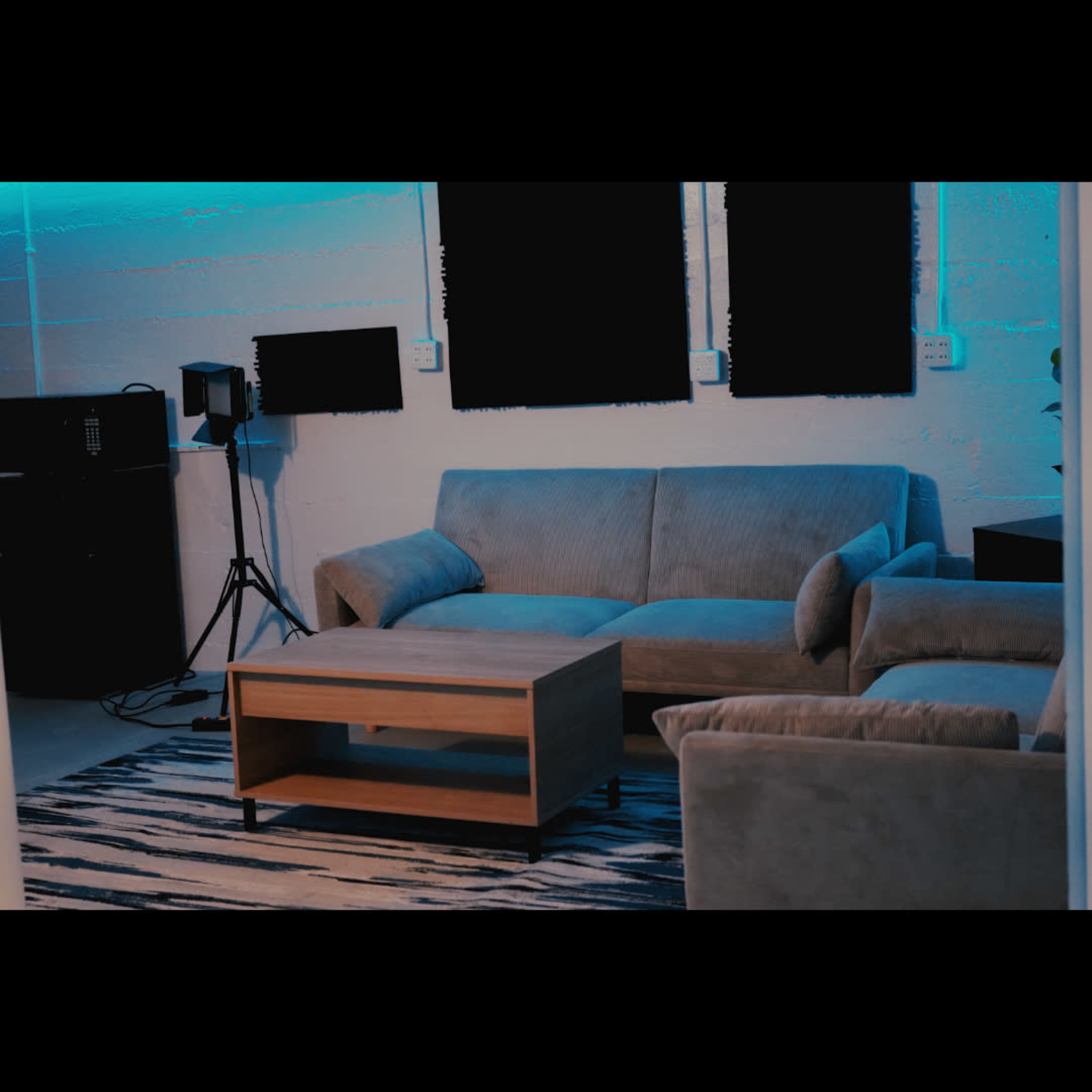 The image shows a modern living room with a beige couch, a wooden coffee table, and a plant, illuminated by blue lighting.