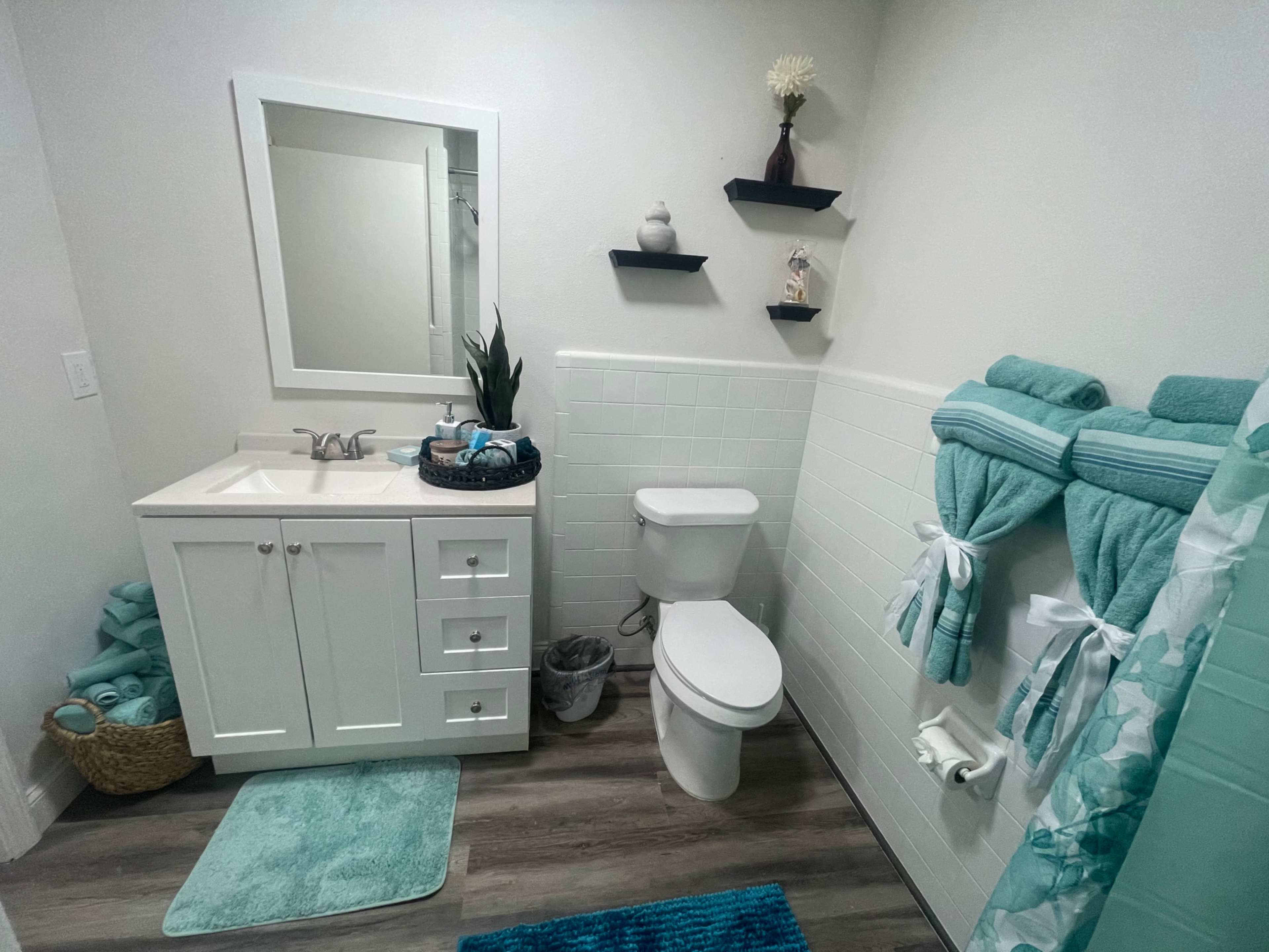 A well-organized bathroom featuring a white vanity, a toilet, teal towels, and decorative shelves with plants and accessories.