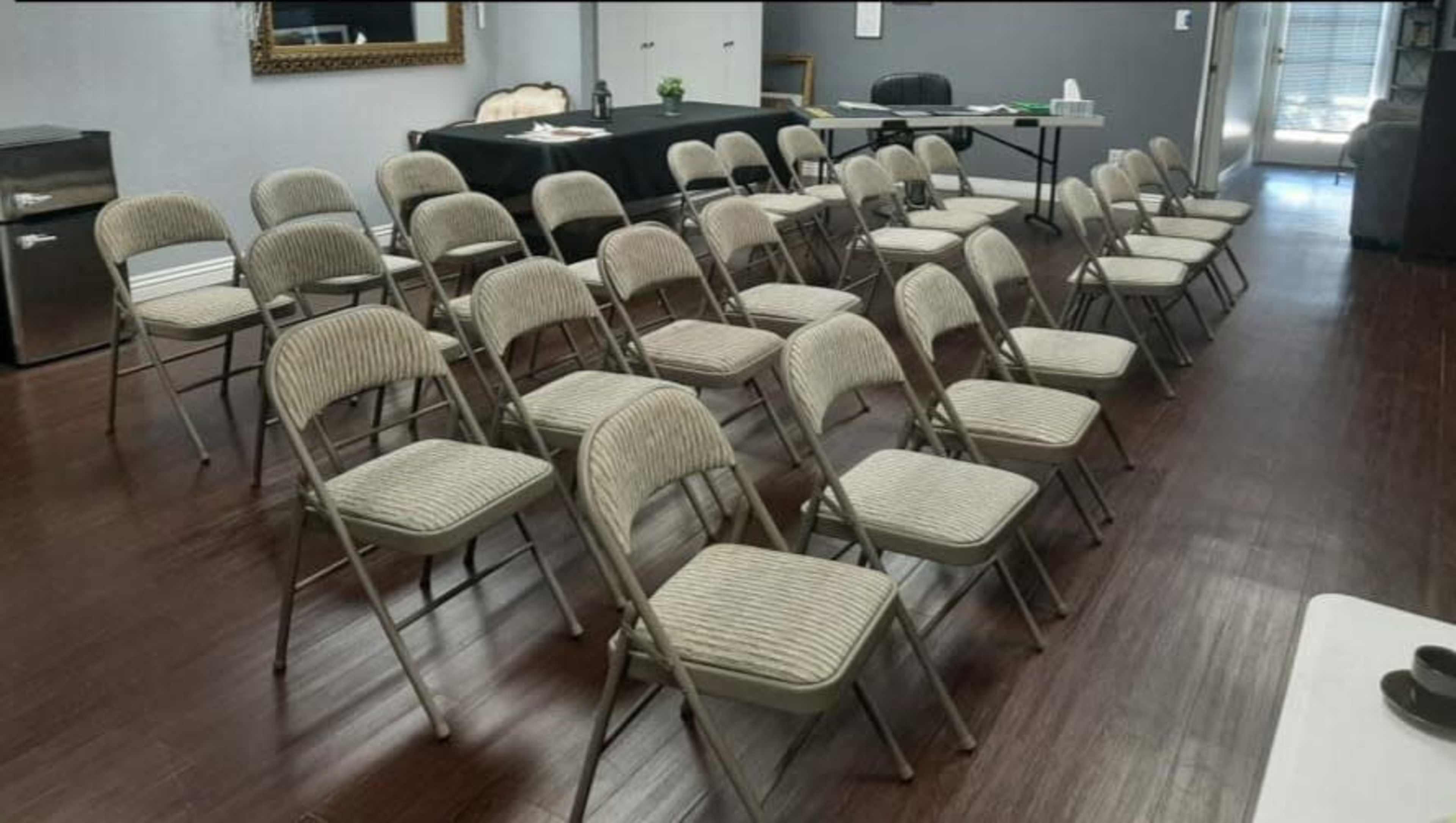 A room arranged with multiple rows of metal folding chairs facing a table set up for an event.