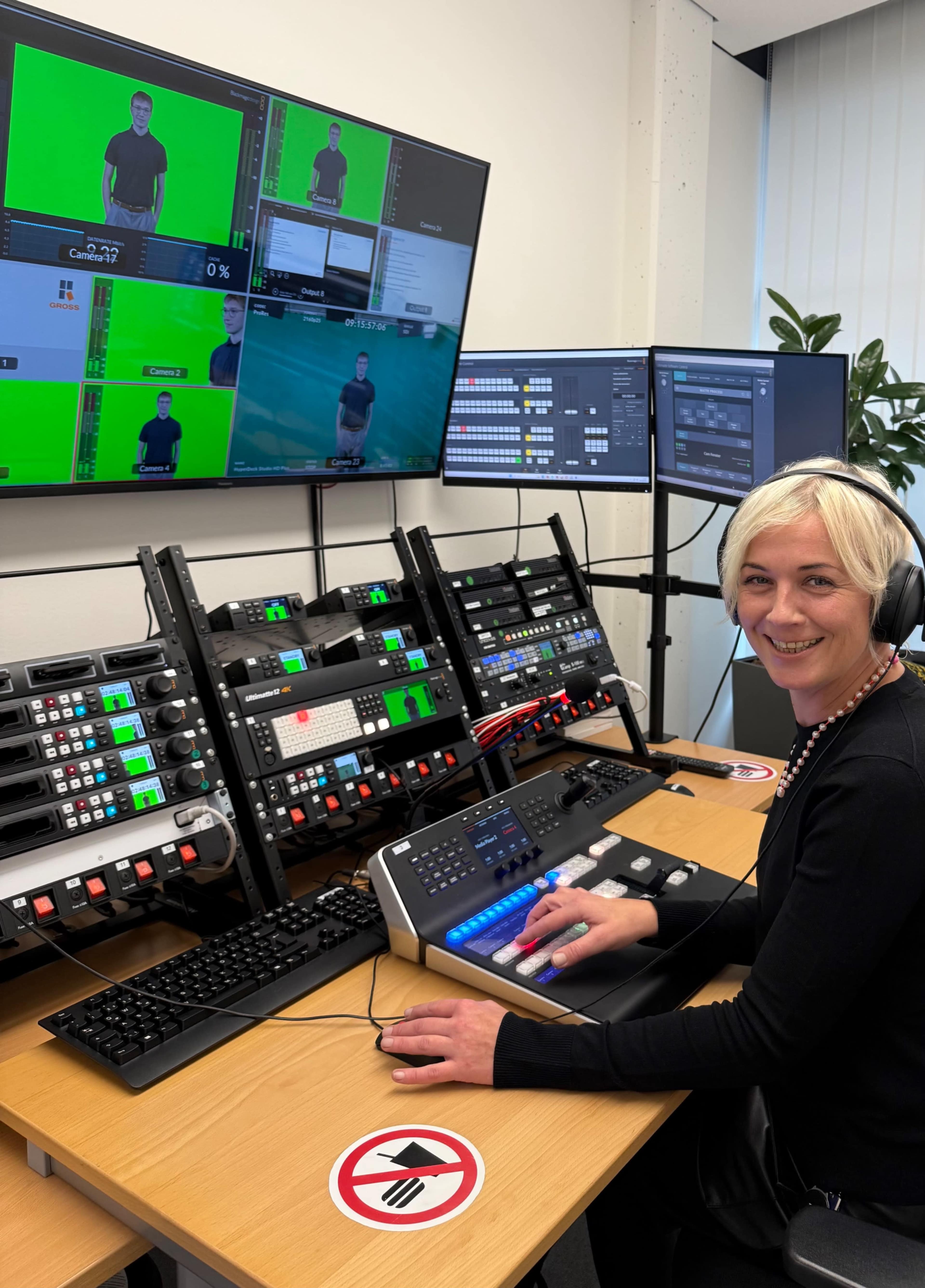 A woman operates a video production control room with multiple monitors and equipment in a well-lit space.