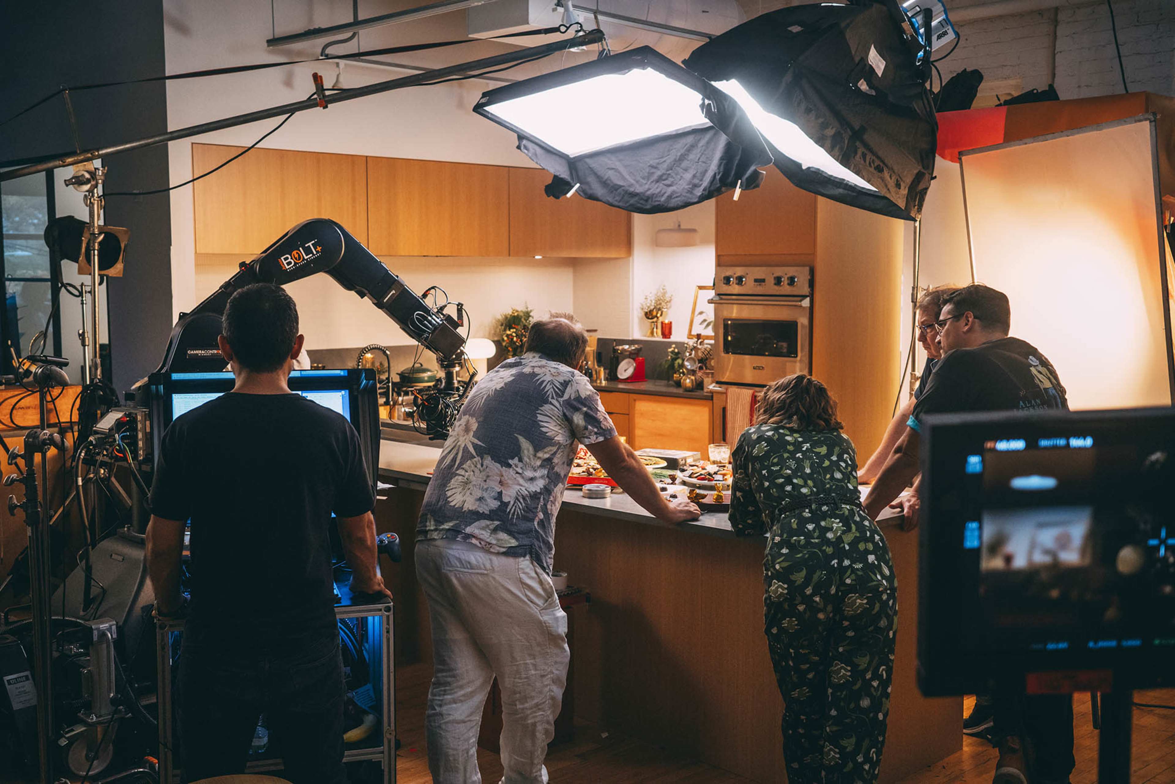 A film crew is gathered around a kitchen set, preparing for a shoot as they assess food arrangements on a countertop.