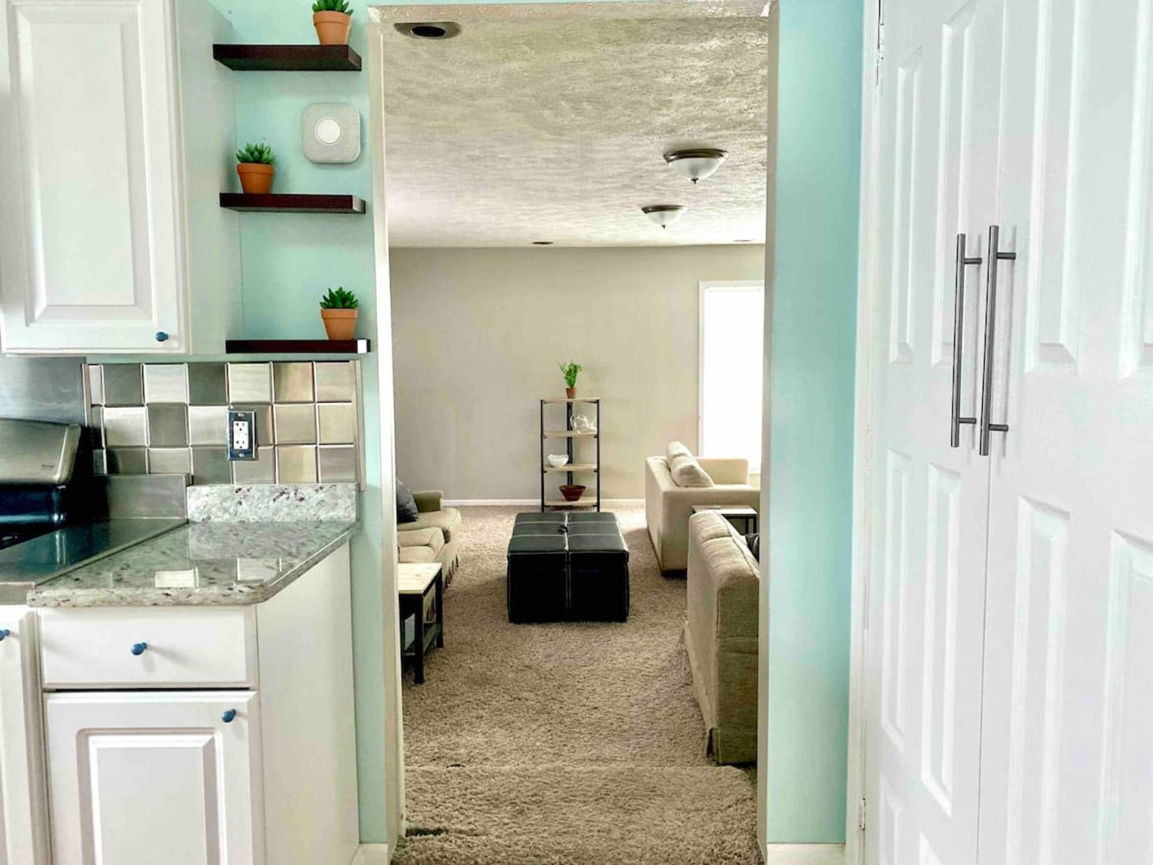 A view from a kitchen into a living room with beige furniture and a coffee table, separated by a doorway.