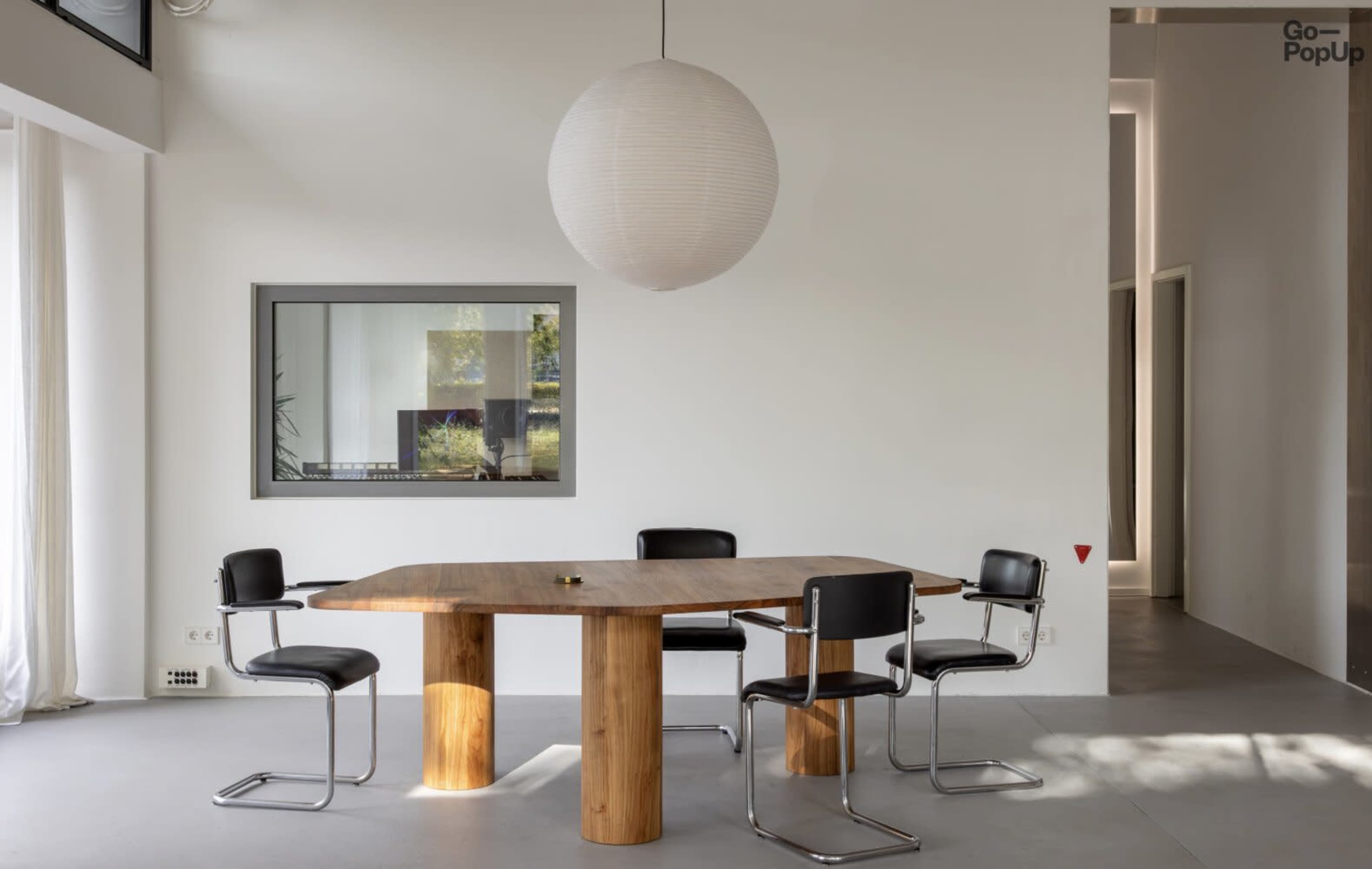 A modern dining area features a wooden table with four black chairs under a round pendant light.