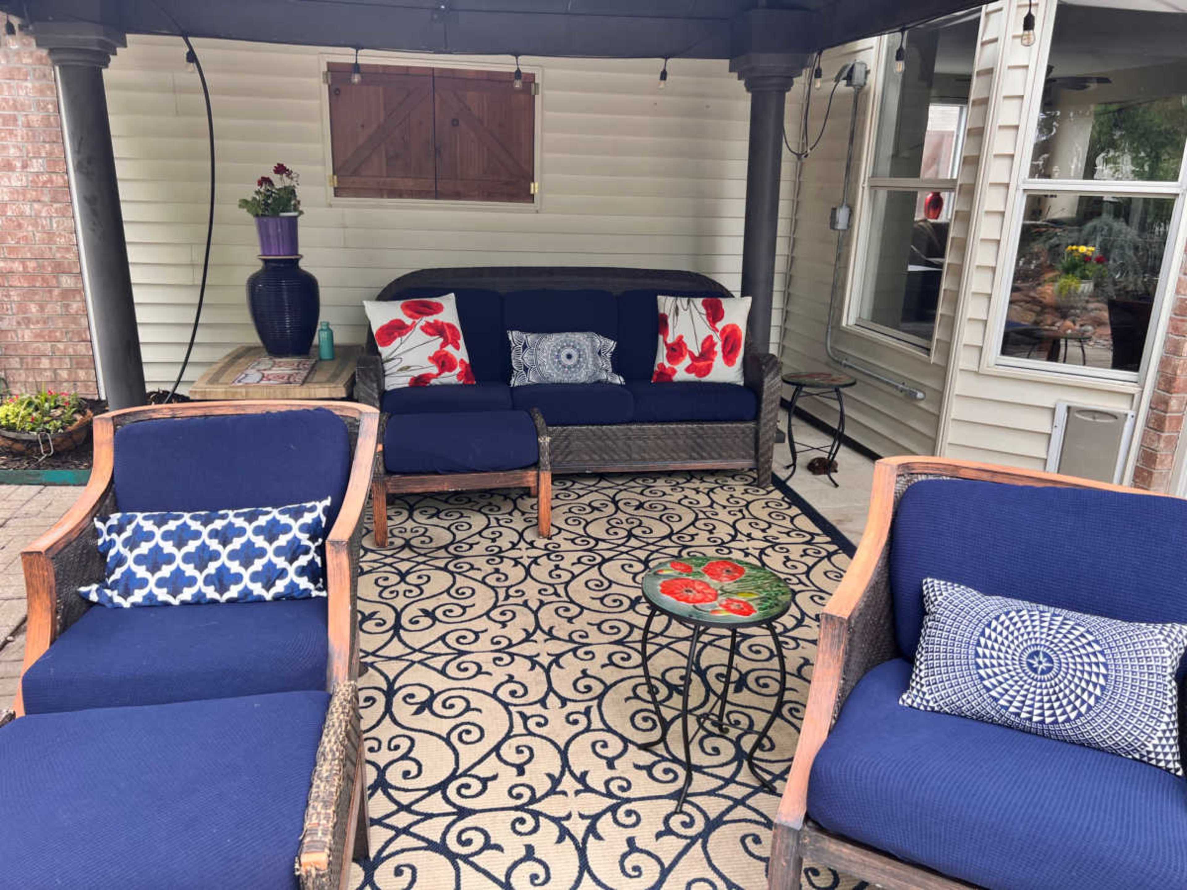 A patio area with a blue couch and armchairs arranged on a patterned rug, surrounded by a brick wall and windows.