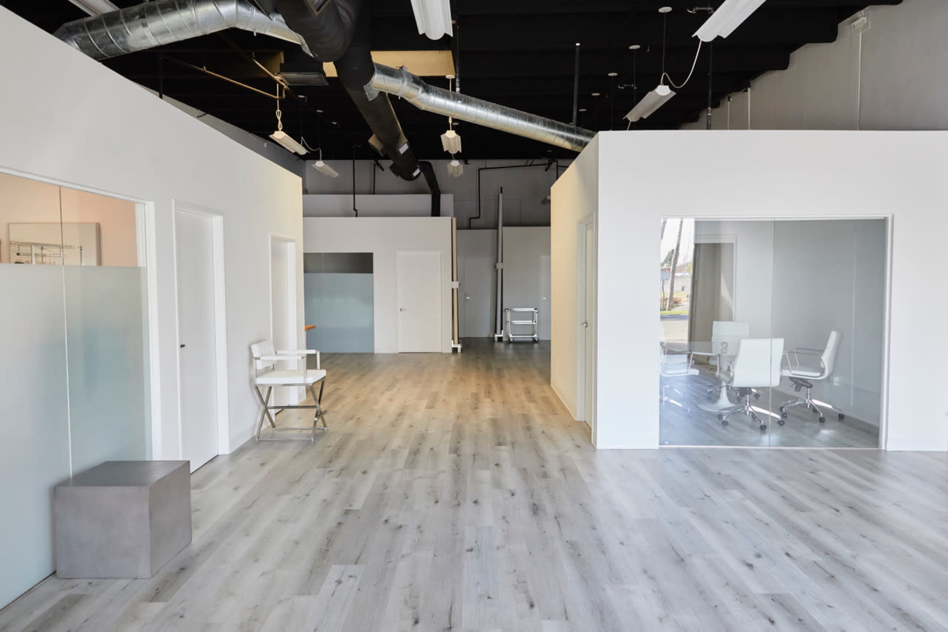 The image shows a modern office space featuring open areas, glass-walled meeting rooms, and minimalist furniture.