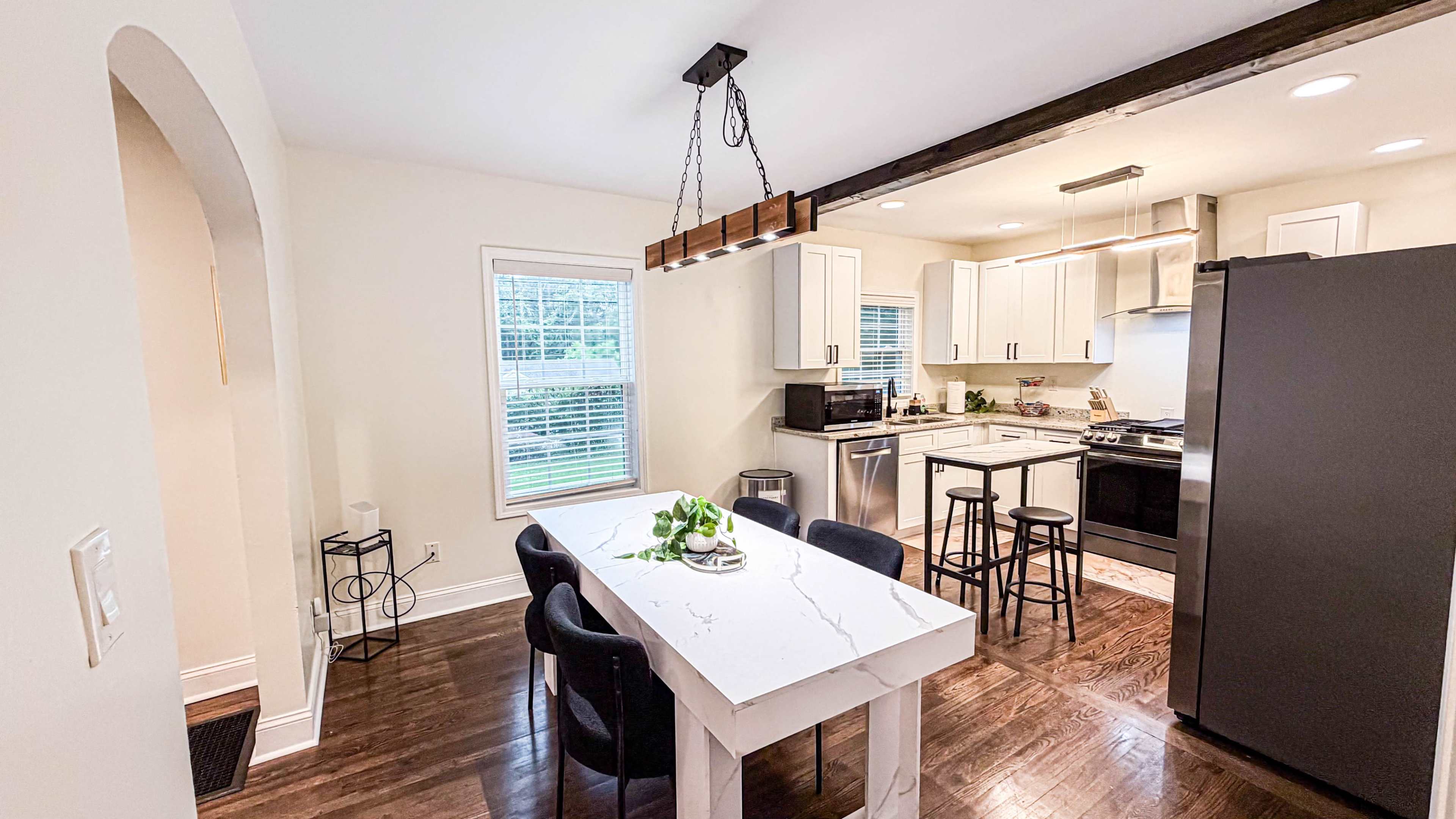 The image shows a modern kitchen and dining area with a marble-top table, black chairs, and stainless steel appliances.