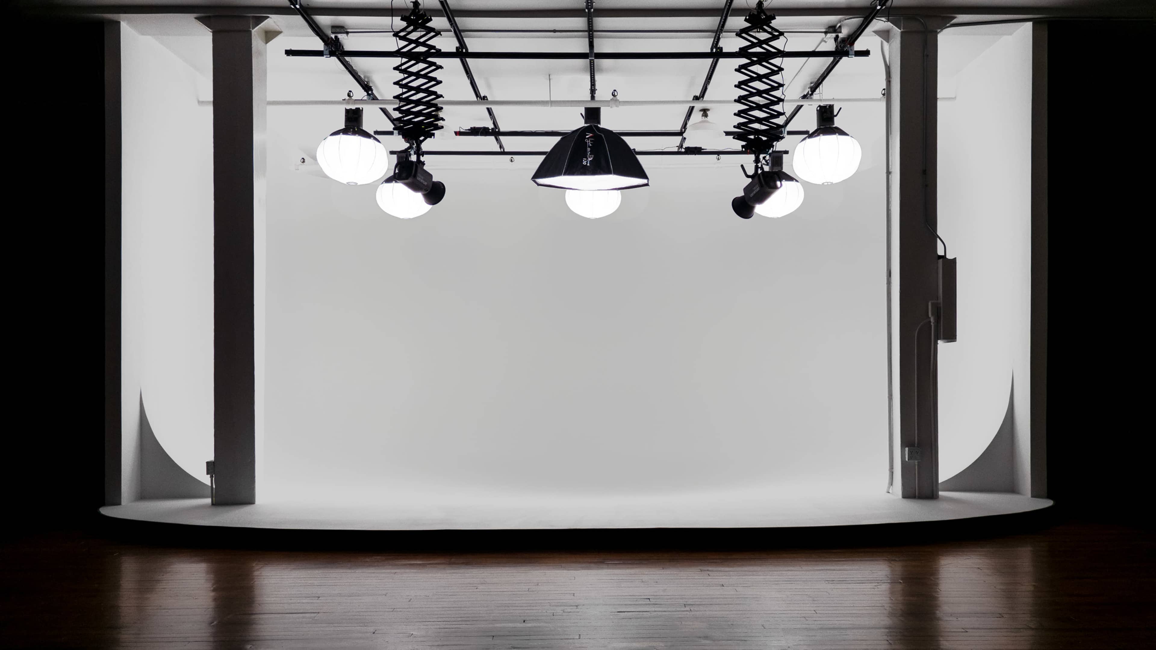The image shows a minimalist studio space with multiple hanging light fixtures above a curved, white backdrop.