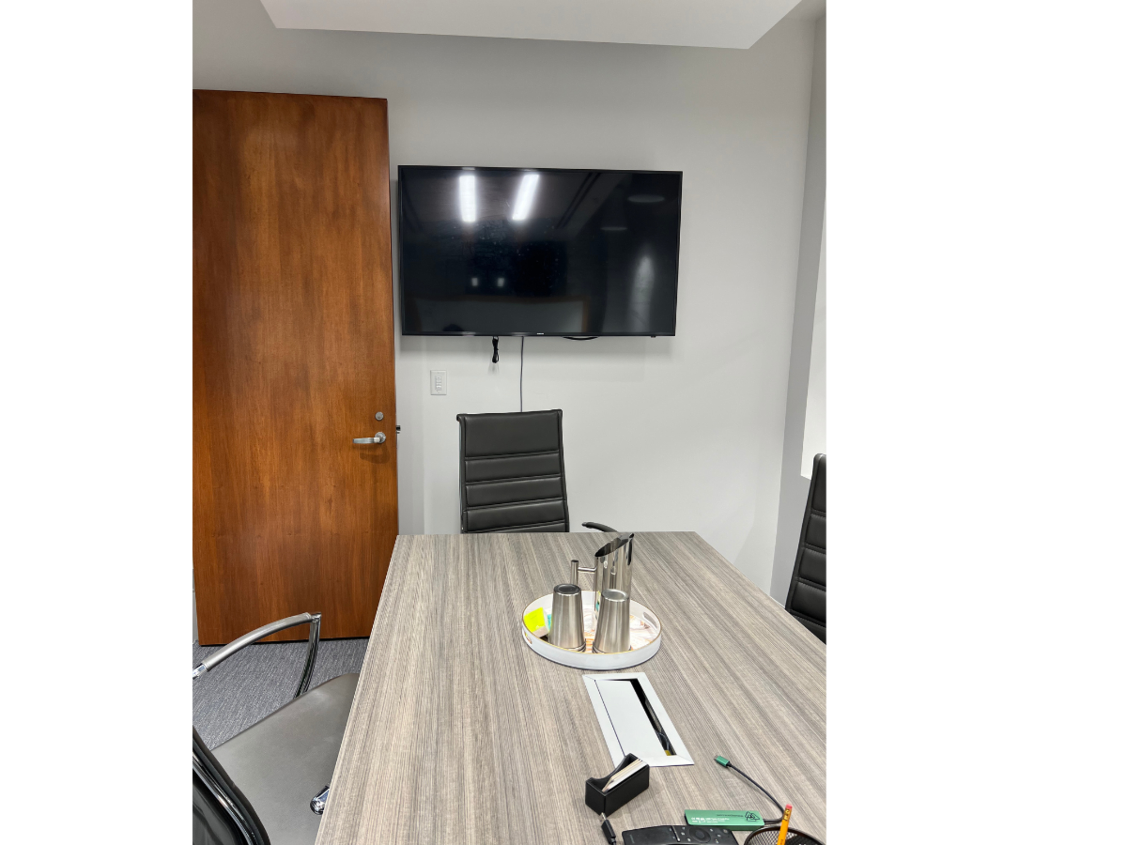 A conference room with a wooden door, a large television mounted on the wall, and a table set with a few utensils and stationery items.