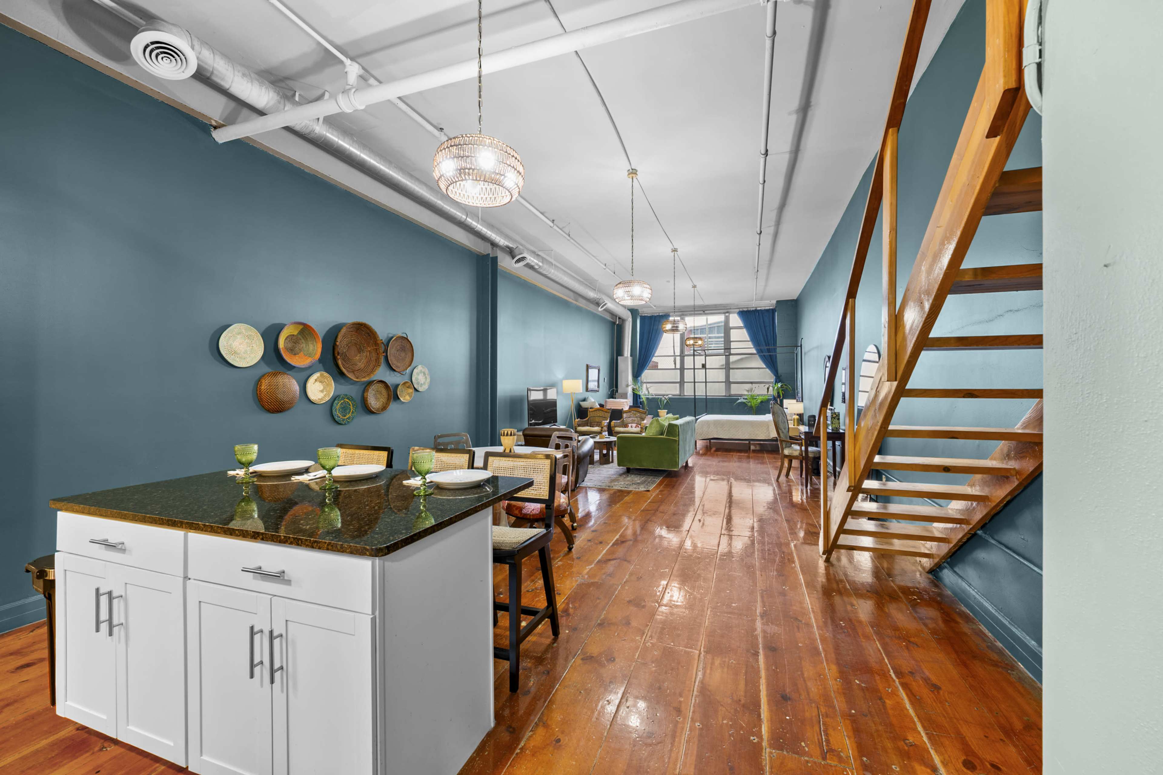 The image shows a spacious living area with a kitchen island, wooden flooring, and a staircase leading to an upper level.