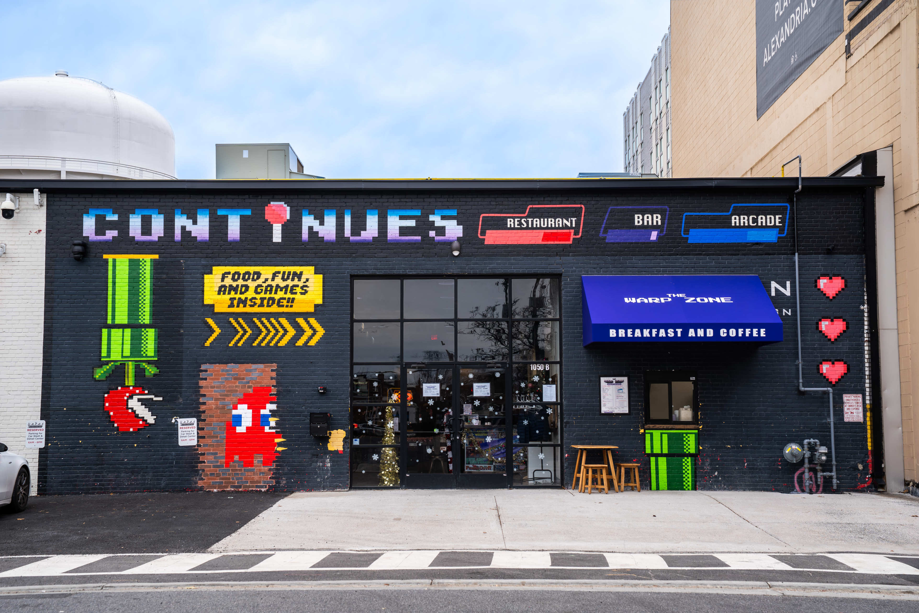 The image shows the exterior of a building with a colorful video game-inspired mural, featuring arcade game characters and signage for a restaurant, bar, and arcade called "Continues."
