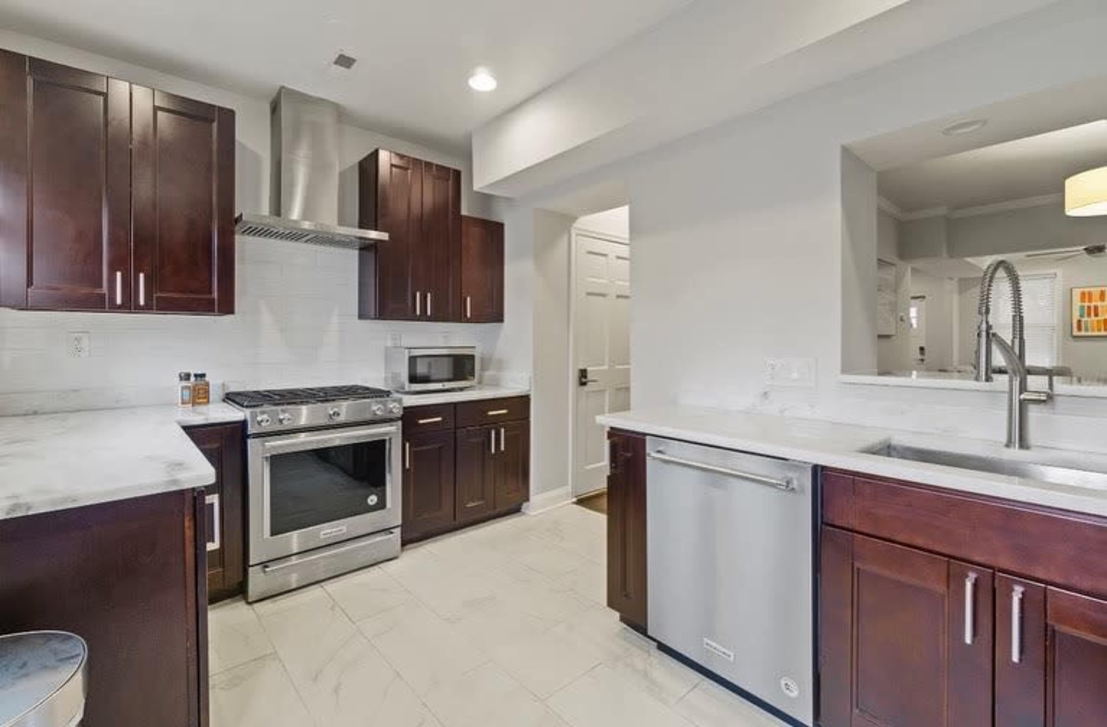 The image shows a modern kitchen featuring dark wood cabinets, stainless steel appliances, and white marble countertops.