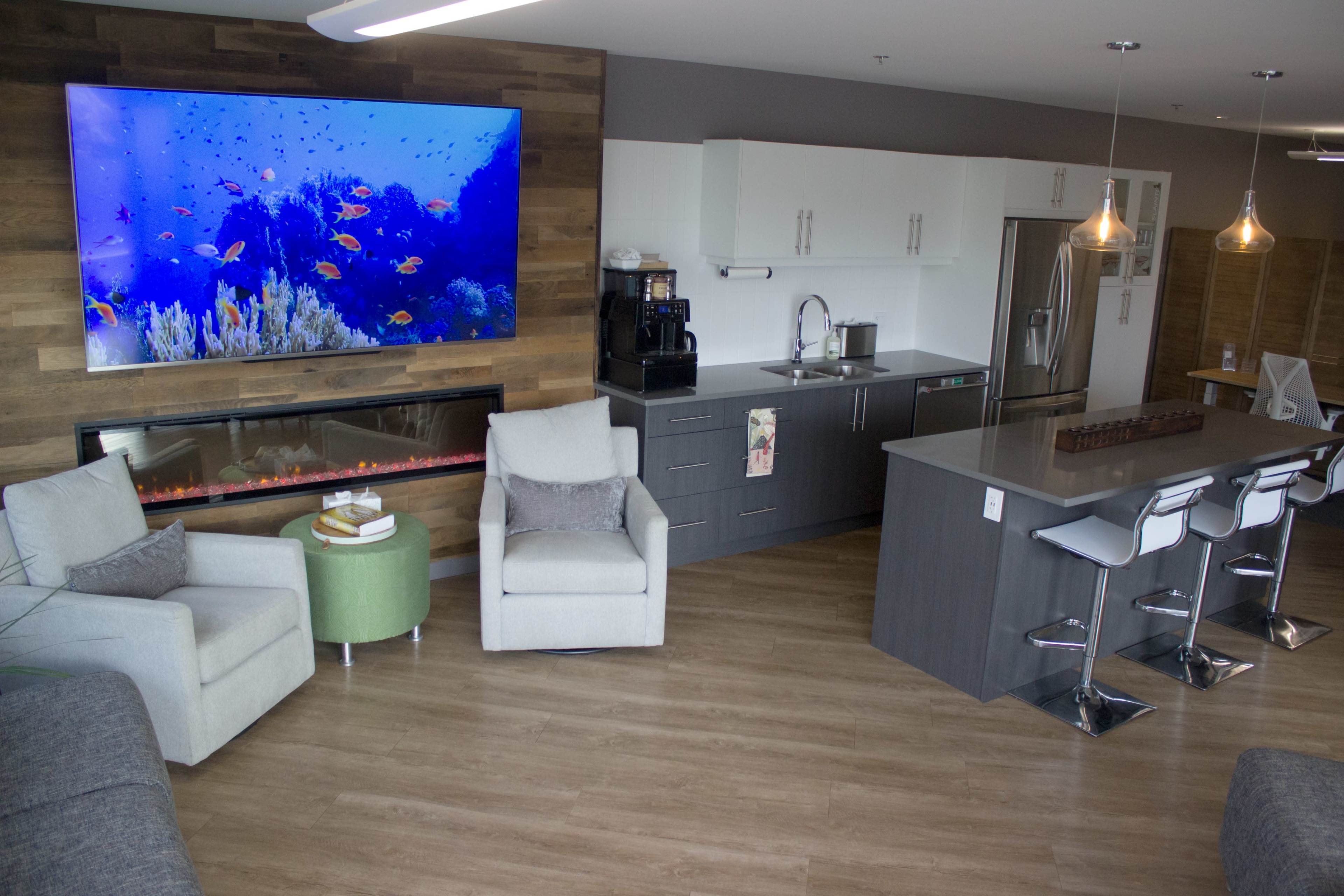 A modern living area features a large aquarium display above a sleek fireplace, with a kitchen and bar area in the background.