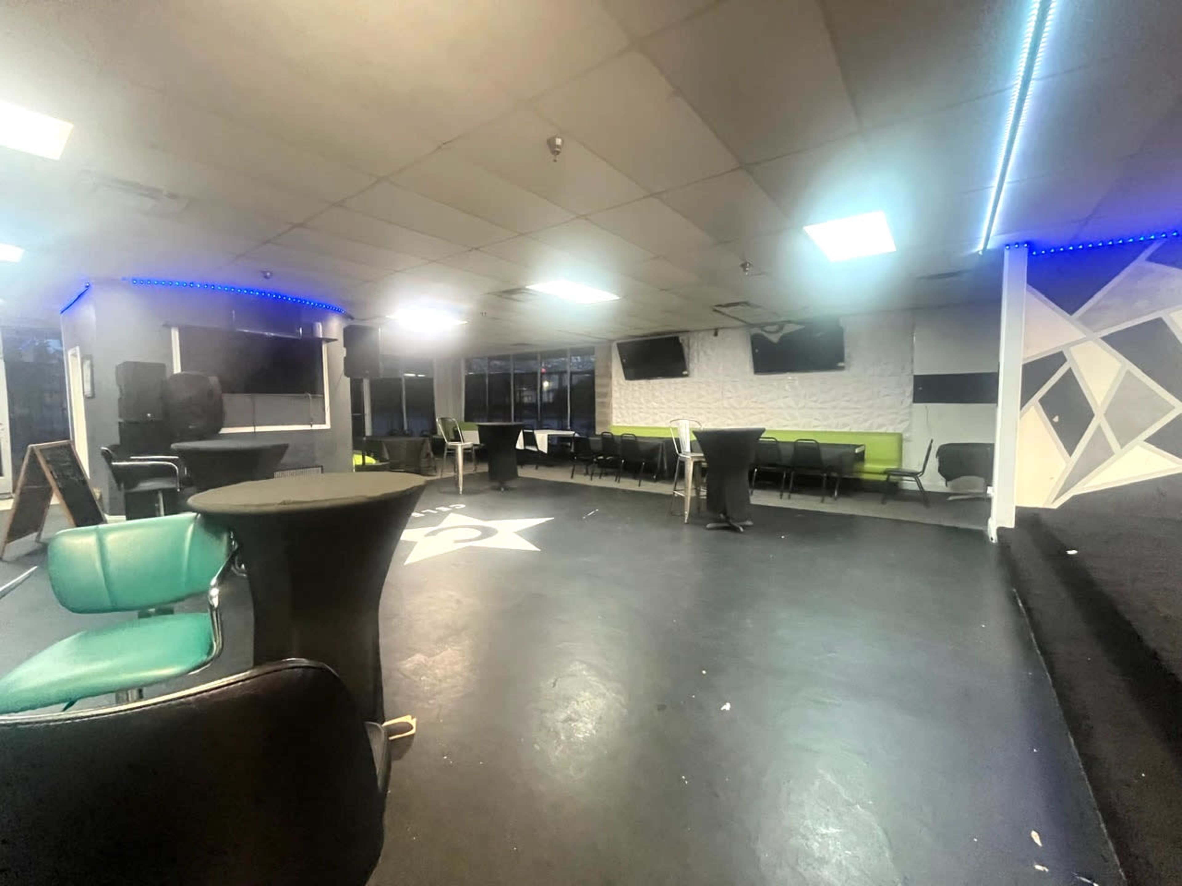 An empty lounge area with a black floor, several tables, chairs, and wall-mounted screens in a well-lit room.