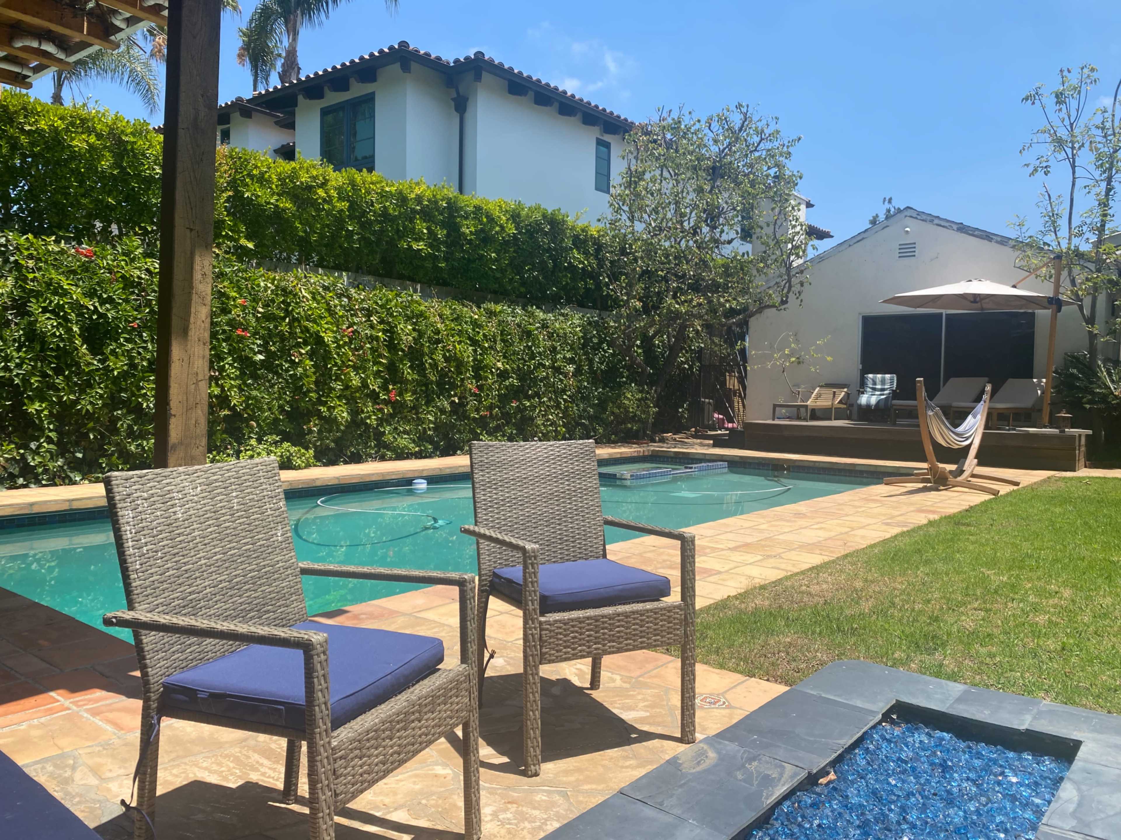The image shows a backyard with a swimming pool, two outdoor chairs, a hammock, and lush greenery surrounding the area.