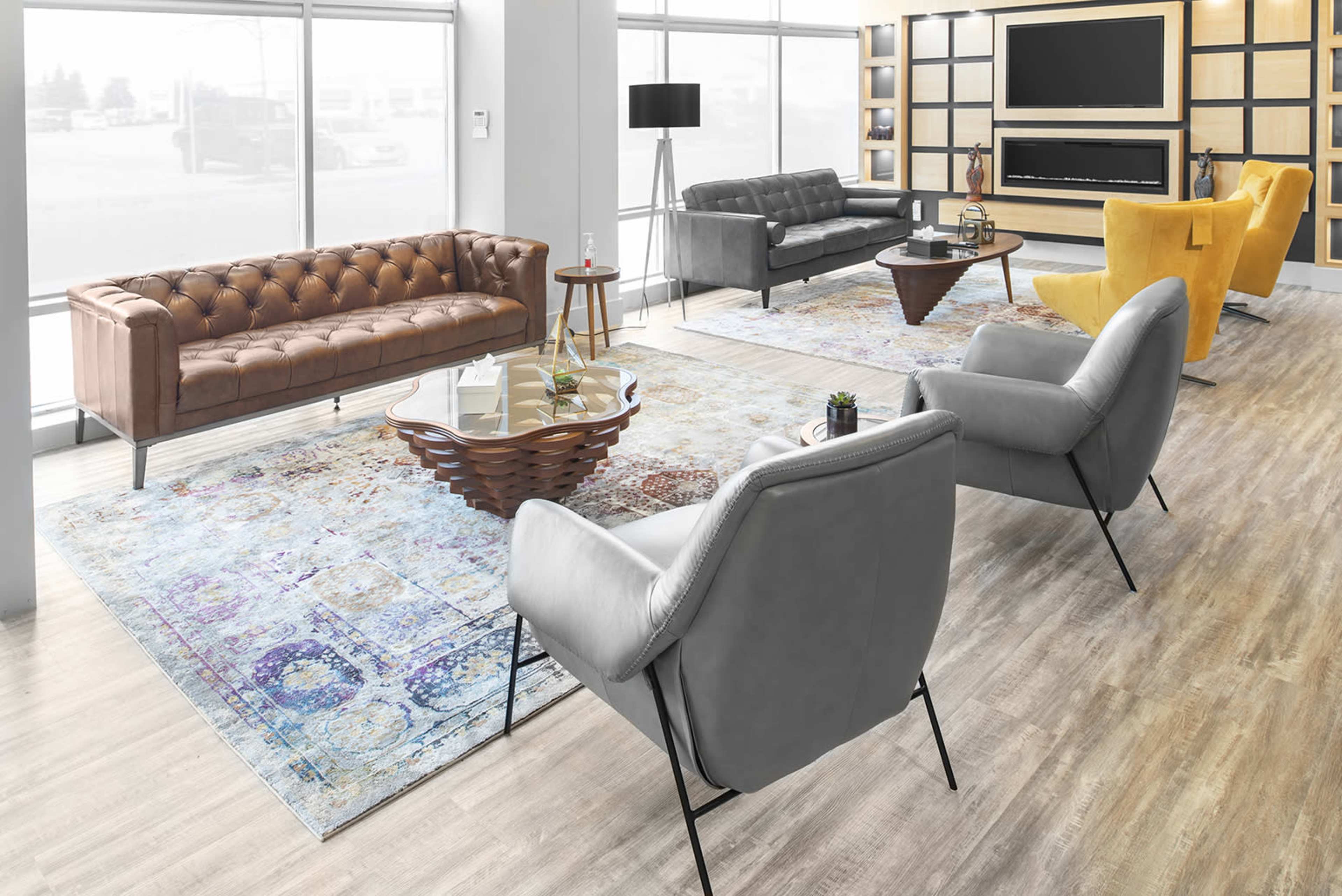 A modern living space with a brown tufted sofa, gray armchairs, a yellow accent chair, a coffee table, and large windows allowing natural light.
