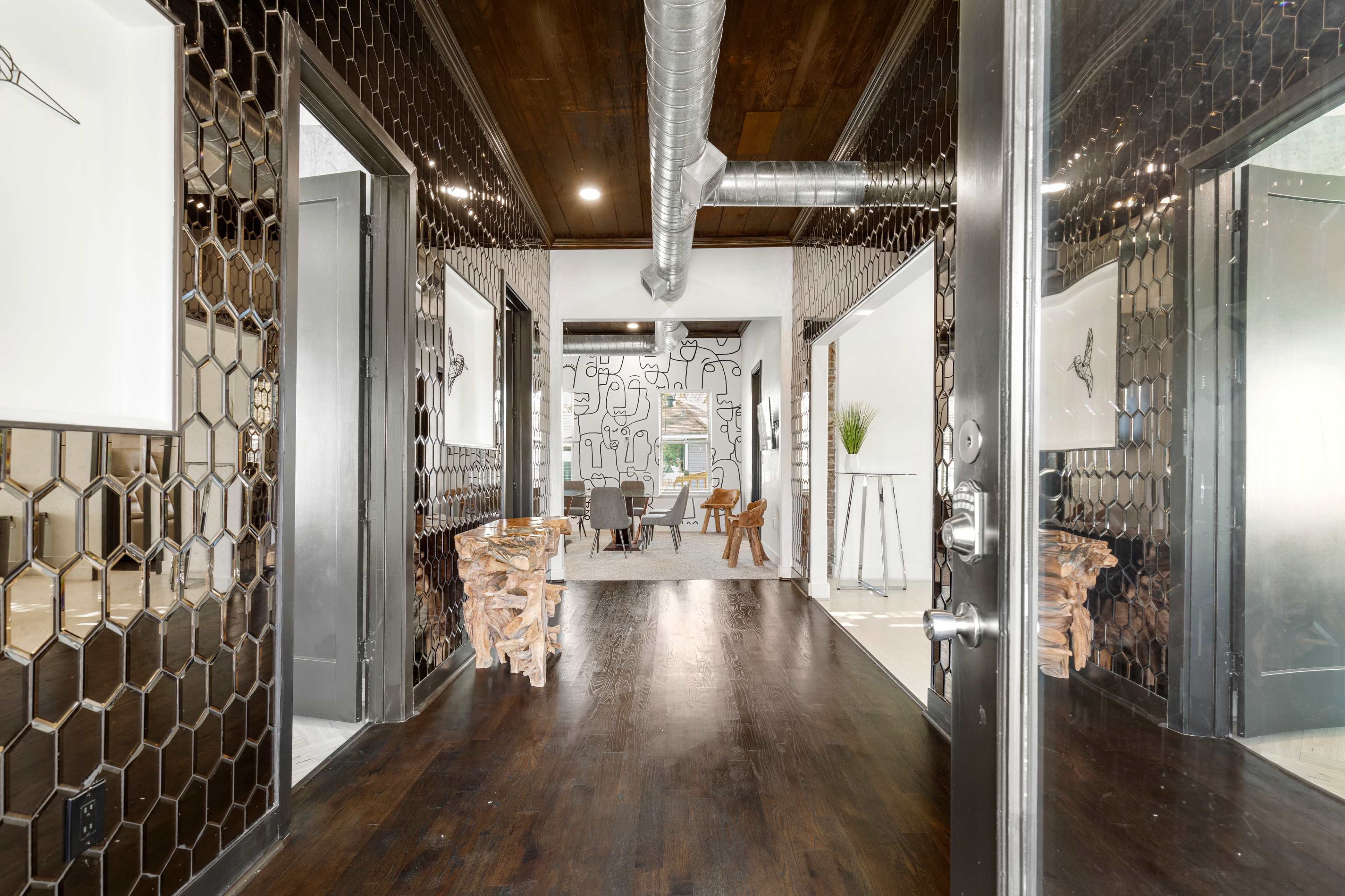 A modern hallway with hexagonal mirrored walls, leading to a furnished room at the end.