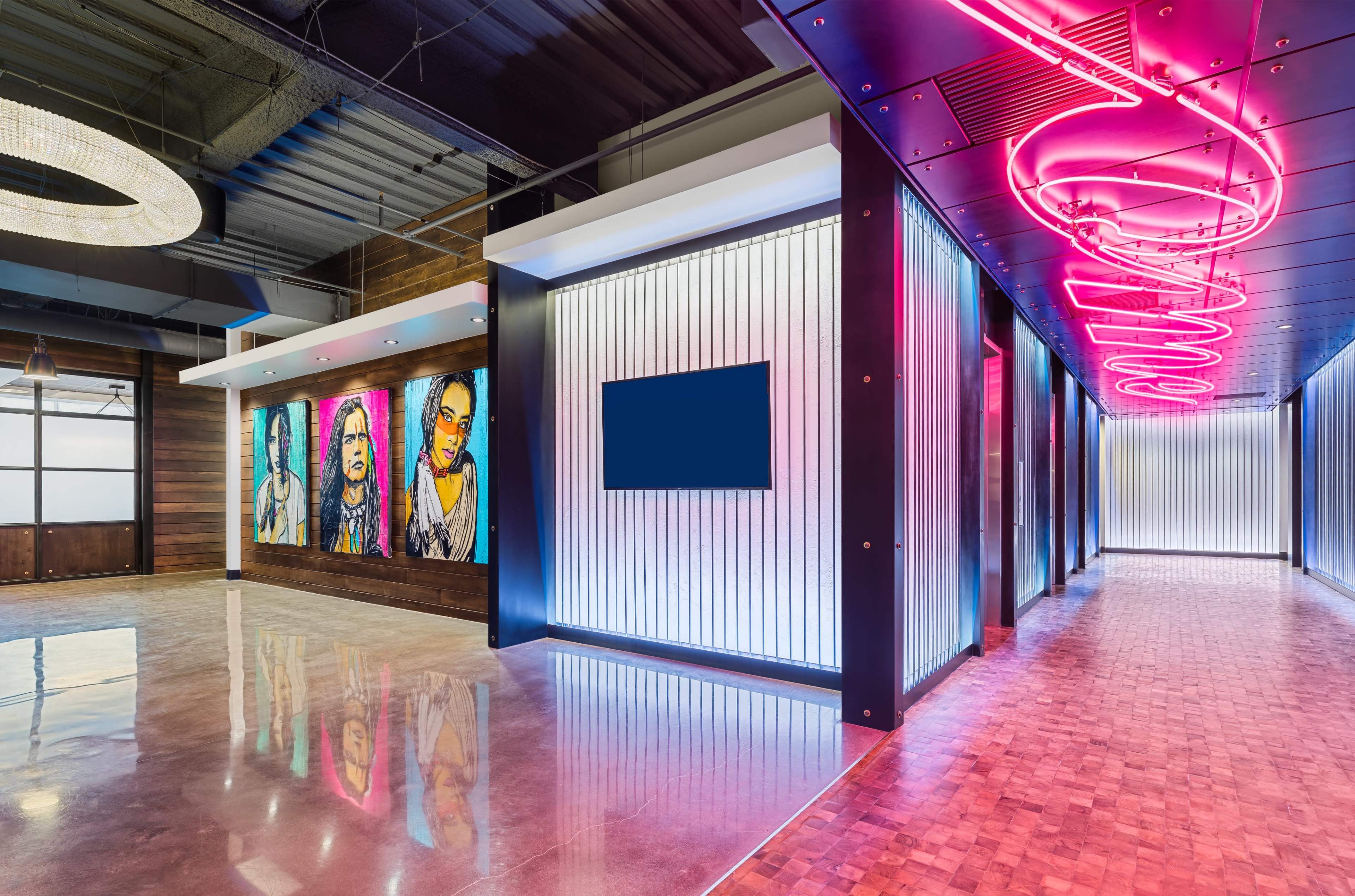 The image shows a modern hallway with vibrant murals on one wall and neon lighting along the ceiling, leading to a clear blue screen on another wall.