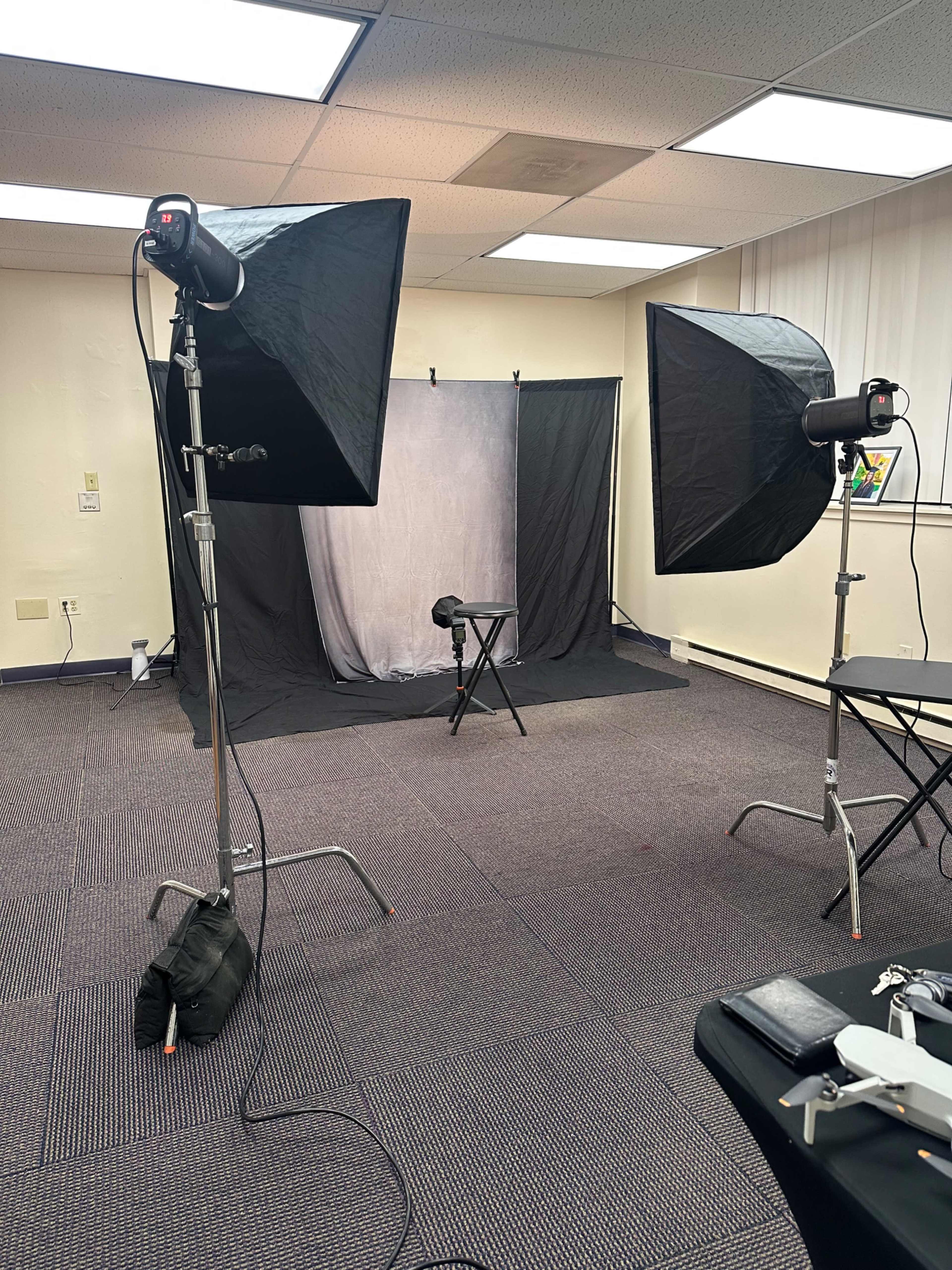 The image shows a photography studio set up with two softbox lights, a backdrop, and a stool positioned in front of the backdrop.