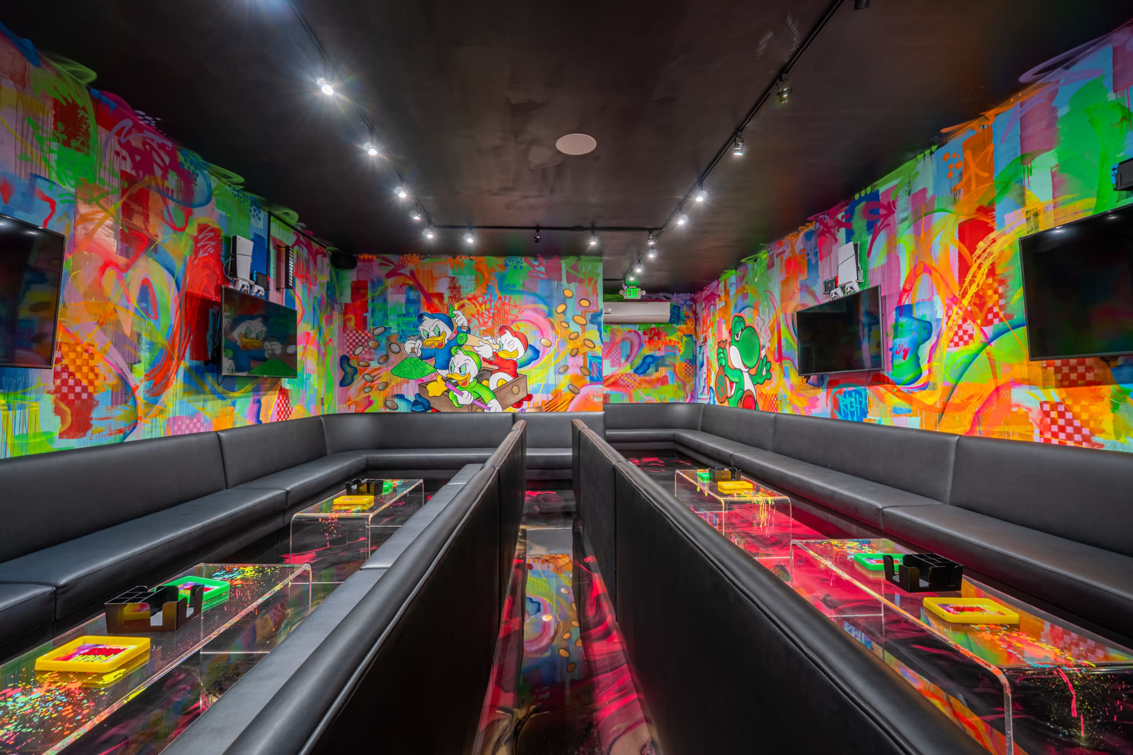 The image shows a vibrant lounge space with multi-colored graffiti on the walls, featuring black seating areas and glass-topped tables.