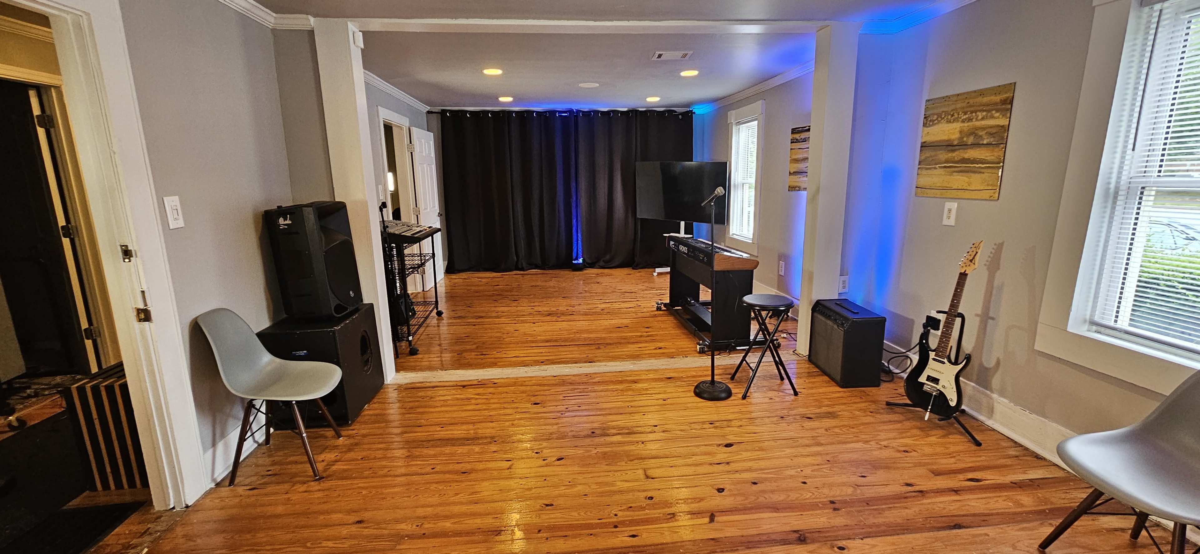 A room with wooden floors, two chairs, a microphone stand, musical equipment, and a black backdrop with lighting.