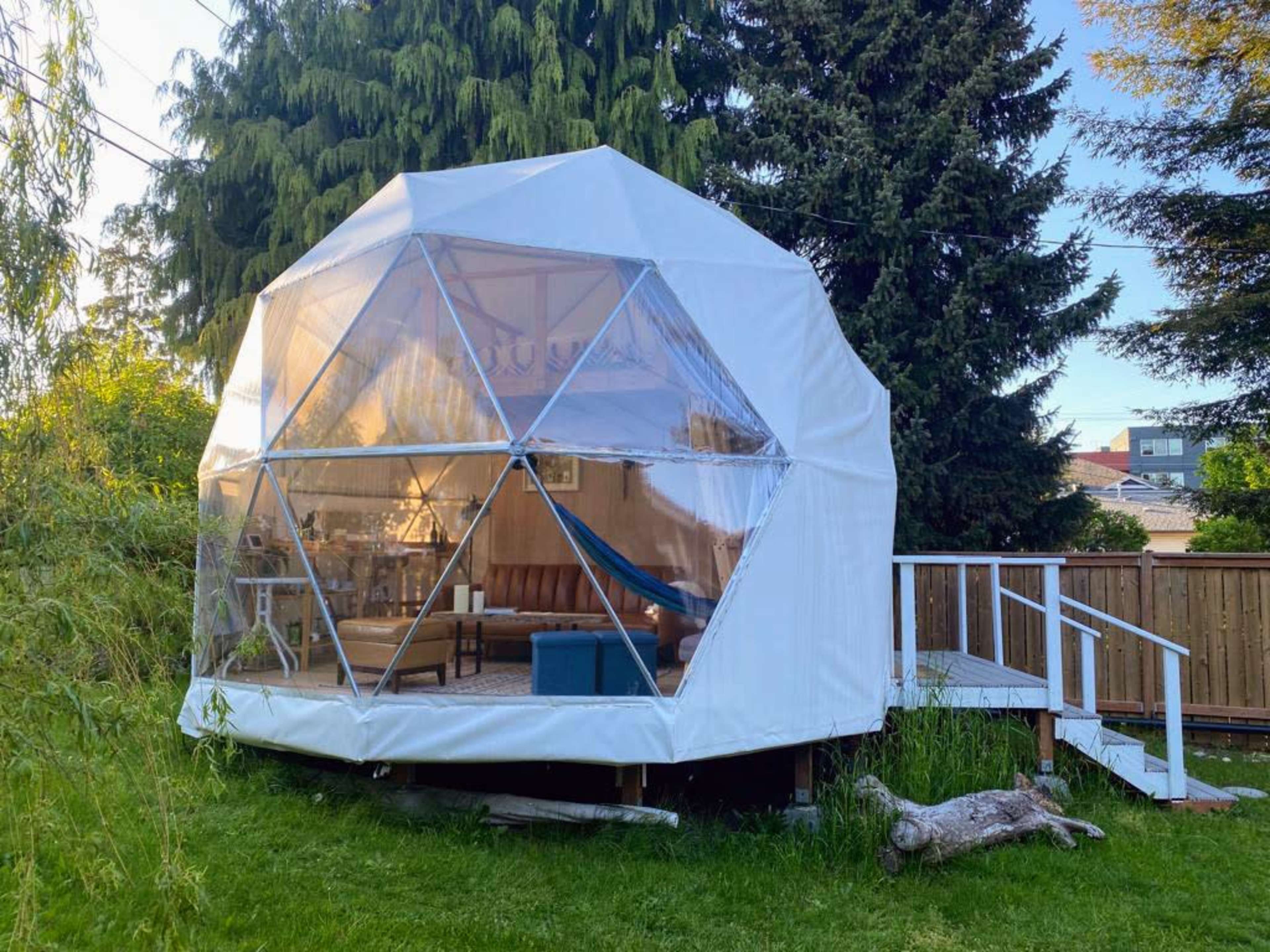 A geodesic dome structure in a backyard, featuring clear panels and a wooden deck with steps.