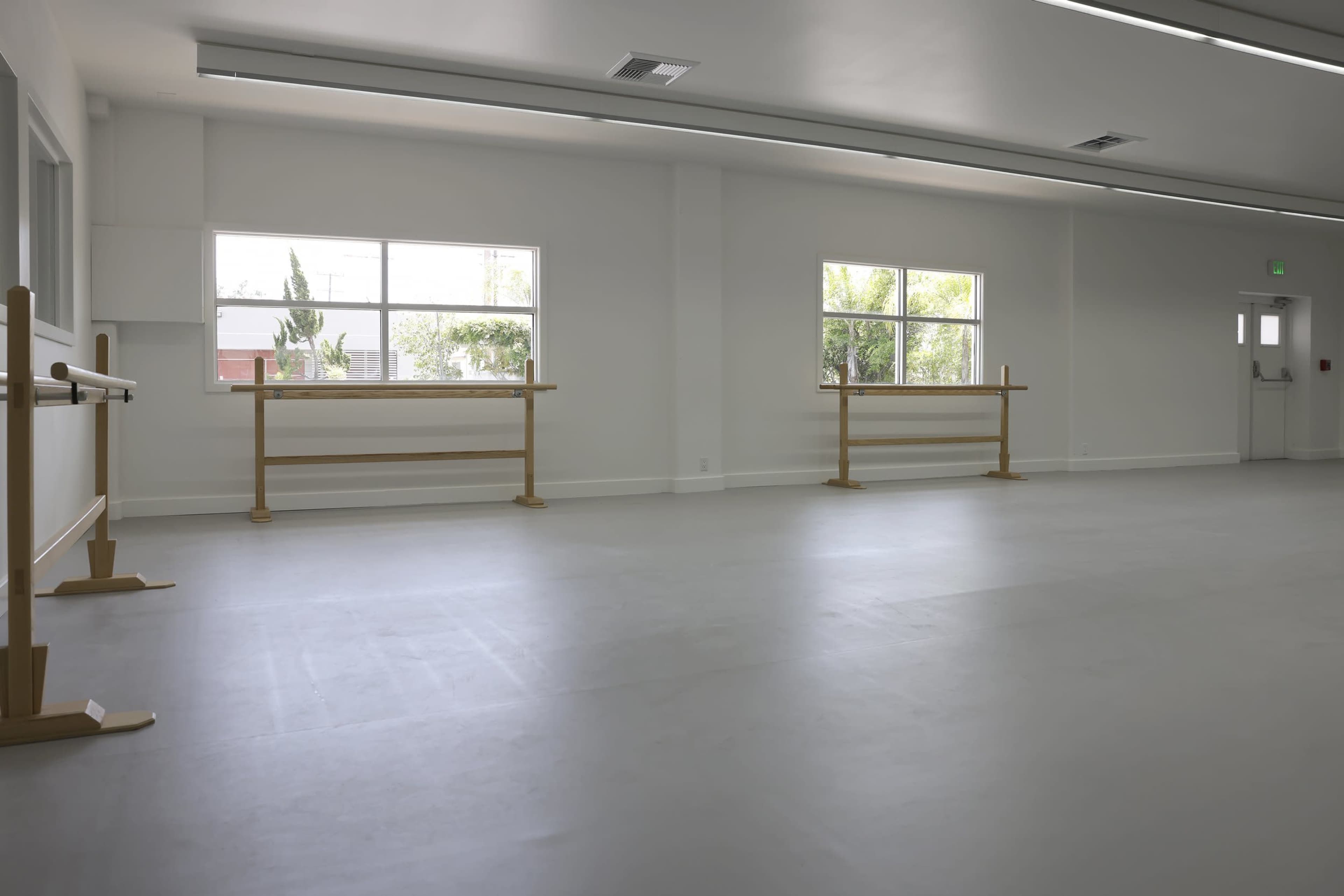 A spacious, empty dance studio with wooden ballet barres along the walls and large windows letting in natural light.