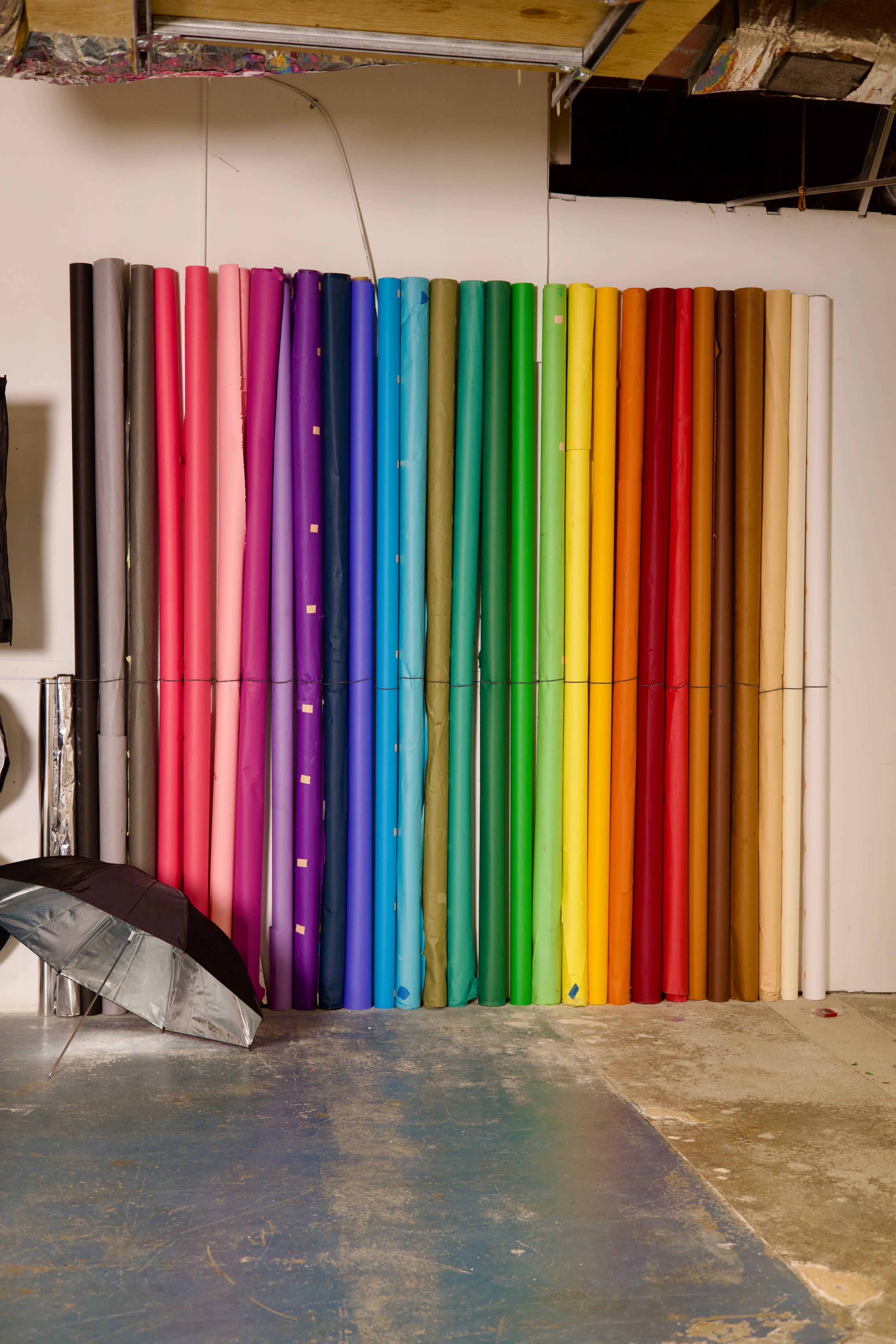 A wall with neatly arranged rolls of colorful backdrop paper in various shades.