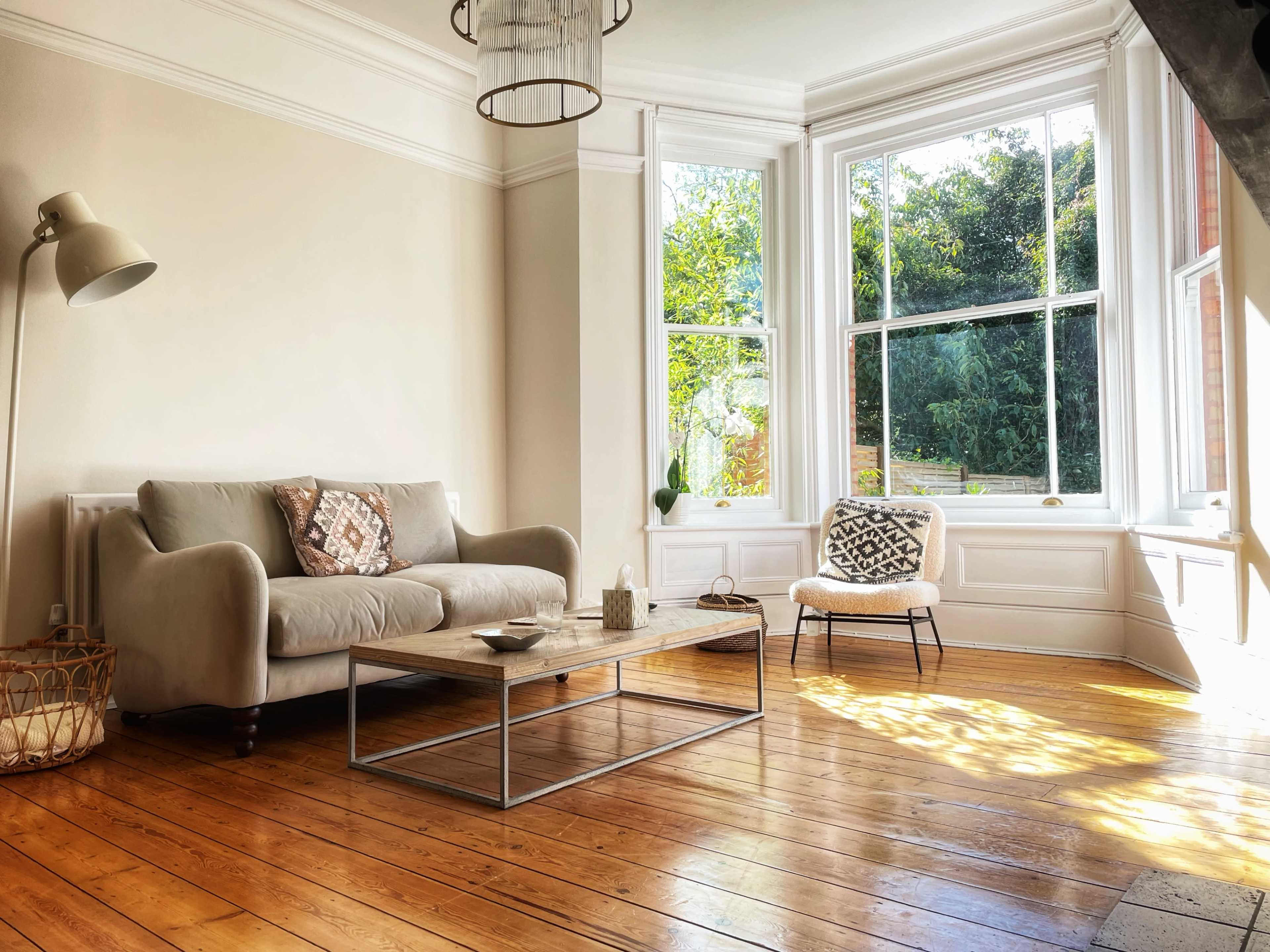 A minimalist living room with a beige sofa, a wooden coffee table, and large windows that allow natural light to flood the space.